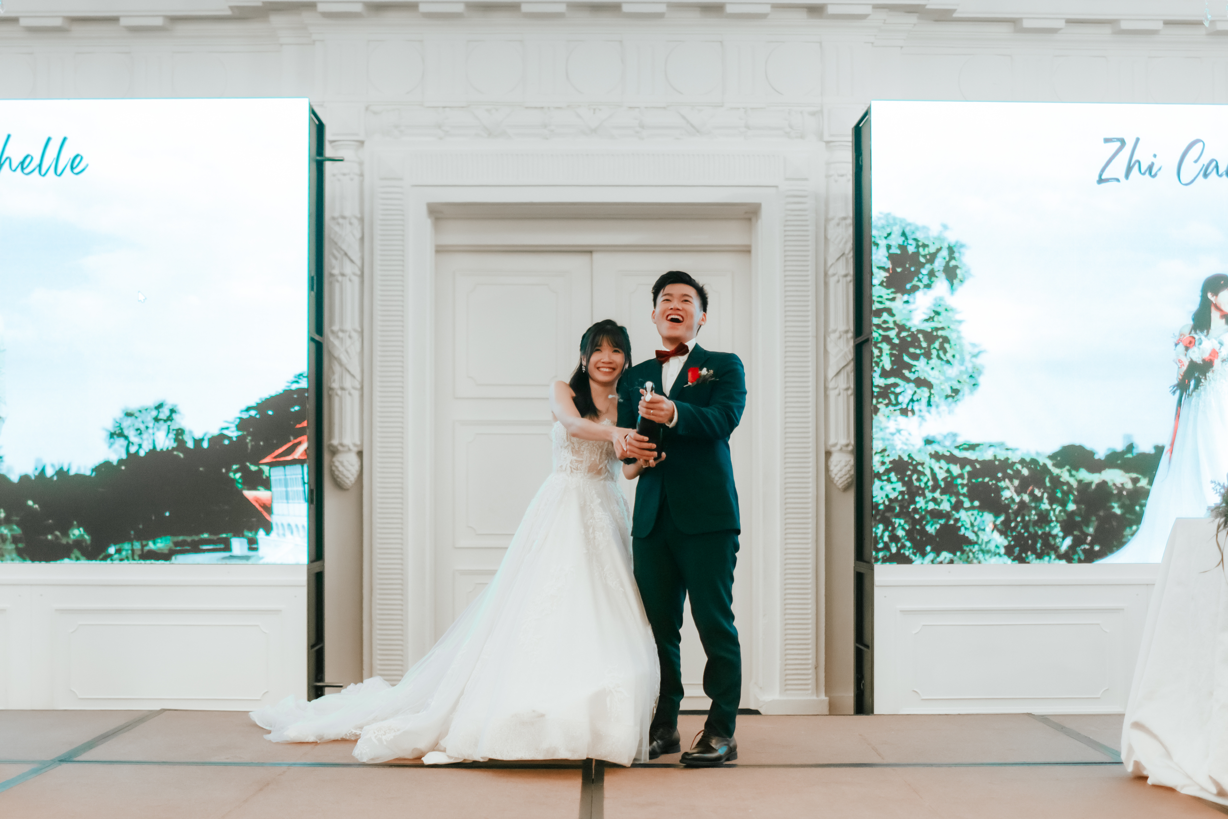 Light and airy actual day wedding photoshoot of the bride and groom popping the cork of a bottle of champagne at The Fullerton Hotel in Singapore. Captured by Arielle for Breadandbutterworks.