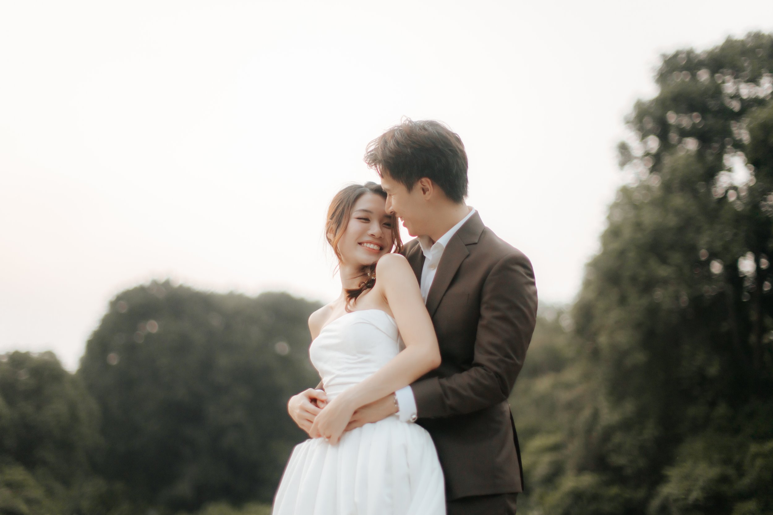 Romantic and dynamic pre-wedding photoshoot at Canterbury Hill. The groom is hugging the bride from the back as they smile at each other lovingly. Captured in a light and airy style by Arielle from Breadandbutterworks.