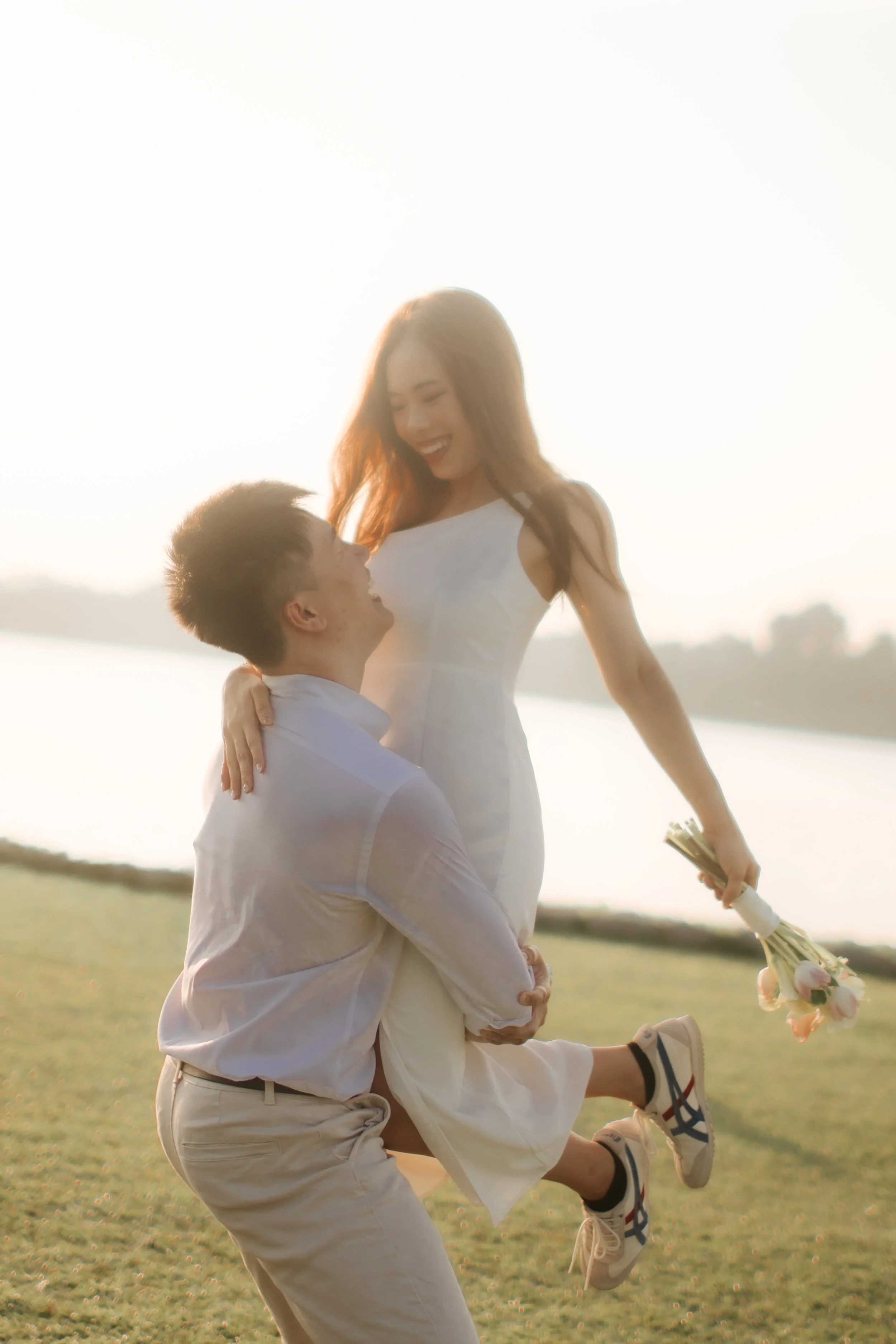 Romantic and airy pre-wedding photoshoot at Upper Seletar Reservoir, the couple is having fun on the grass with sunset as a backdrop. Captured by Arielle from Breadandbutterworks.