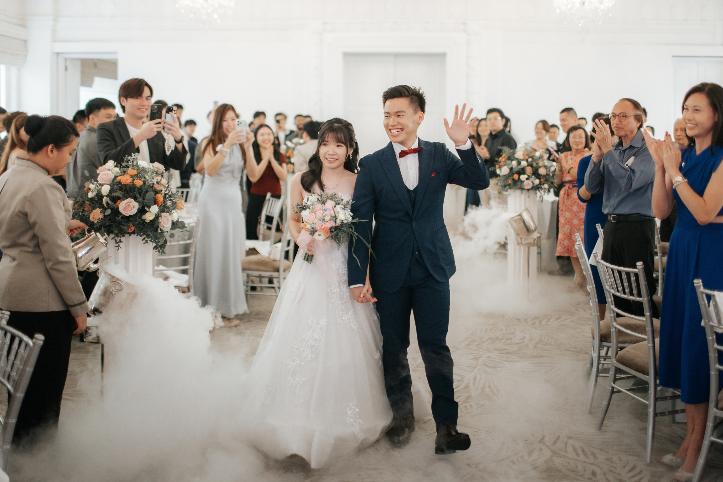 Light and airy actual day wedding photoshoot of the bride and groom walking down the venue at The Fullerton Hotel in Singapore amongst their guests. Captured by Arielle for Breadandbutterworks.