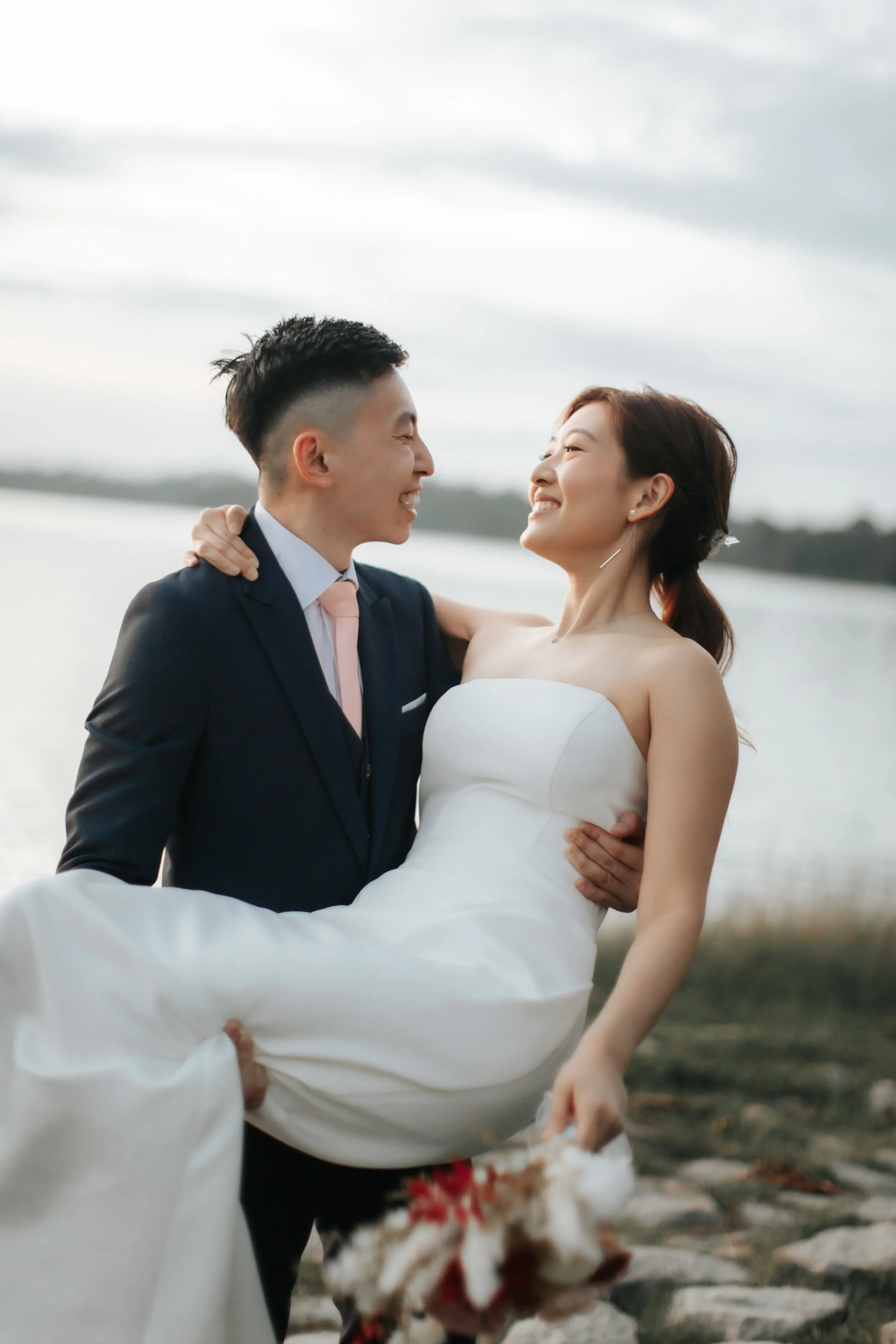 Romantic pre-wedding photoshoot at Upper Seletar Reservoir during golden hour sunset, the groom carries the bride and they exchange a romantic look. Captured in the light and airy style of Breadandbutterworks.