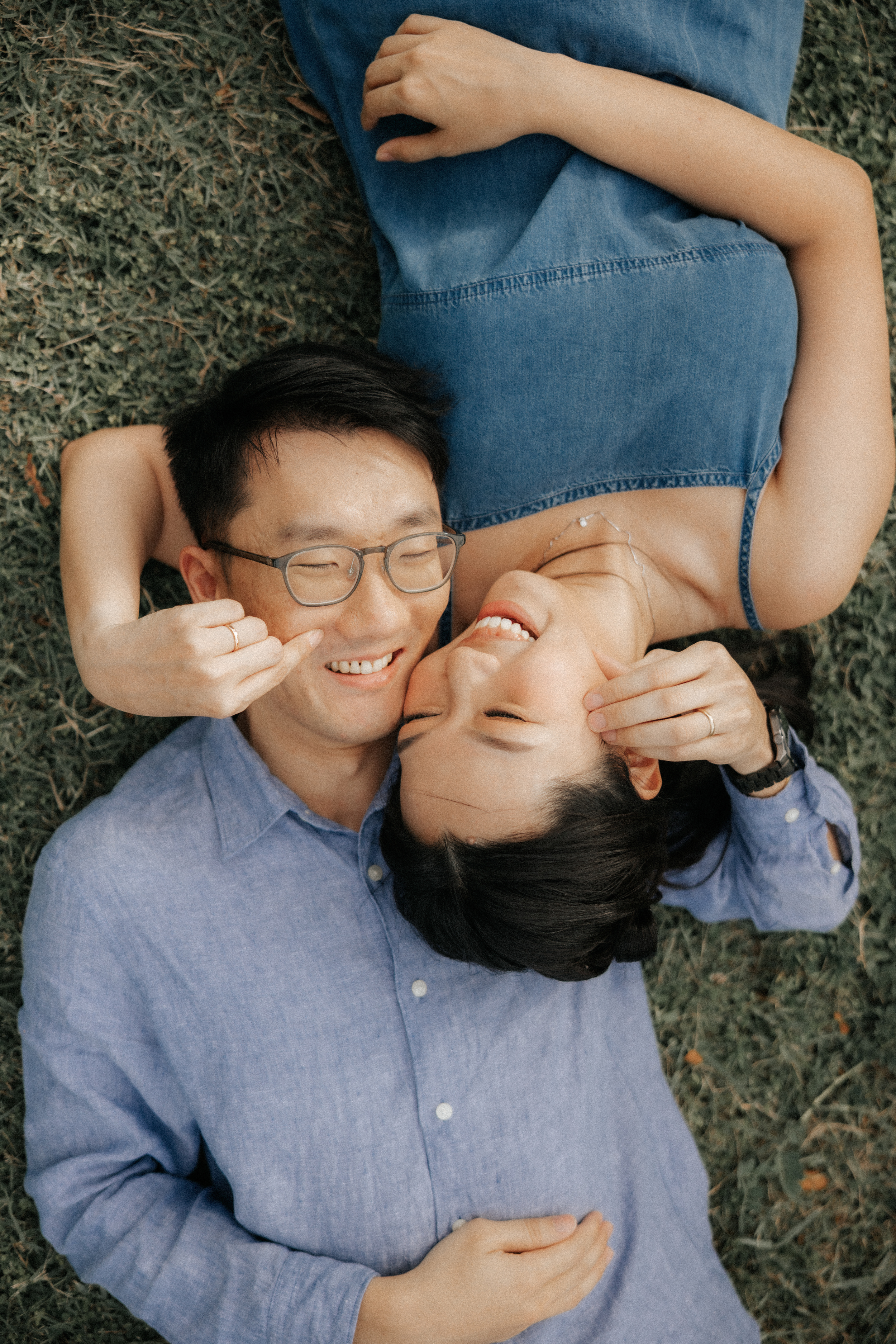 Playful pre-wedding photo of a couple lying together on the grass at East Coast Park, captured by Breadandbutterworks in a soft and heartfelt style.