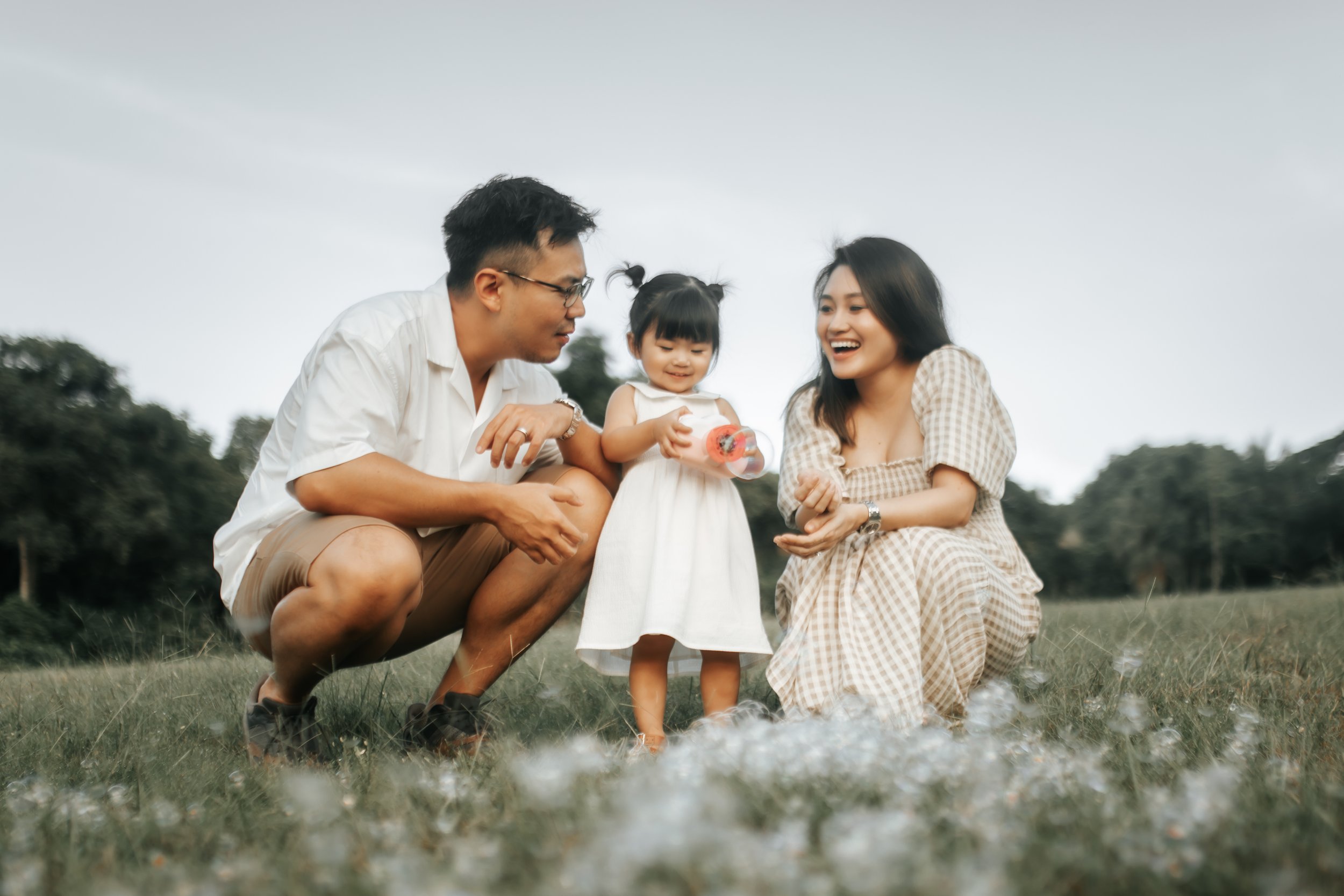 Cover image for Arielle’s family and maternity photography collection, featuring a young family smiling together in a grassy field in Singapore.