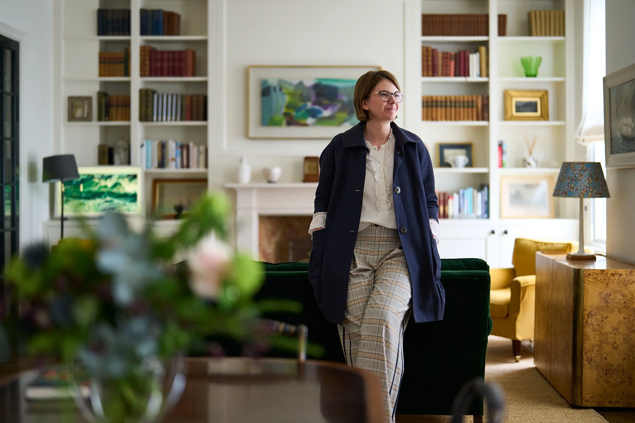 An interior designer  standing in a cozy, well-decorated living room with fitted shelving, artwork, and lamps.