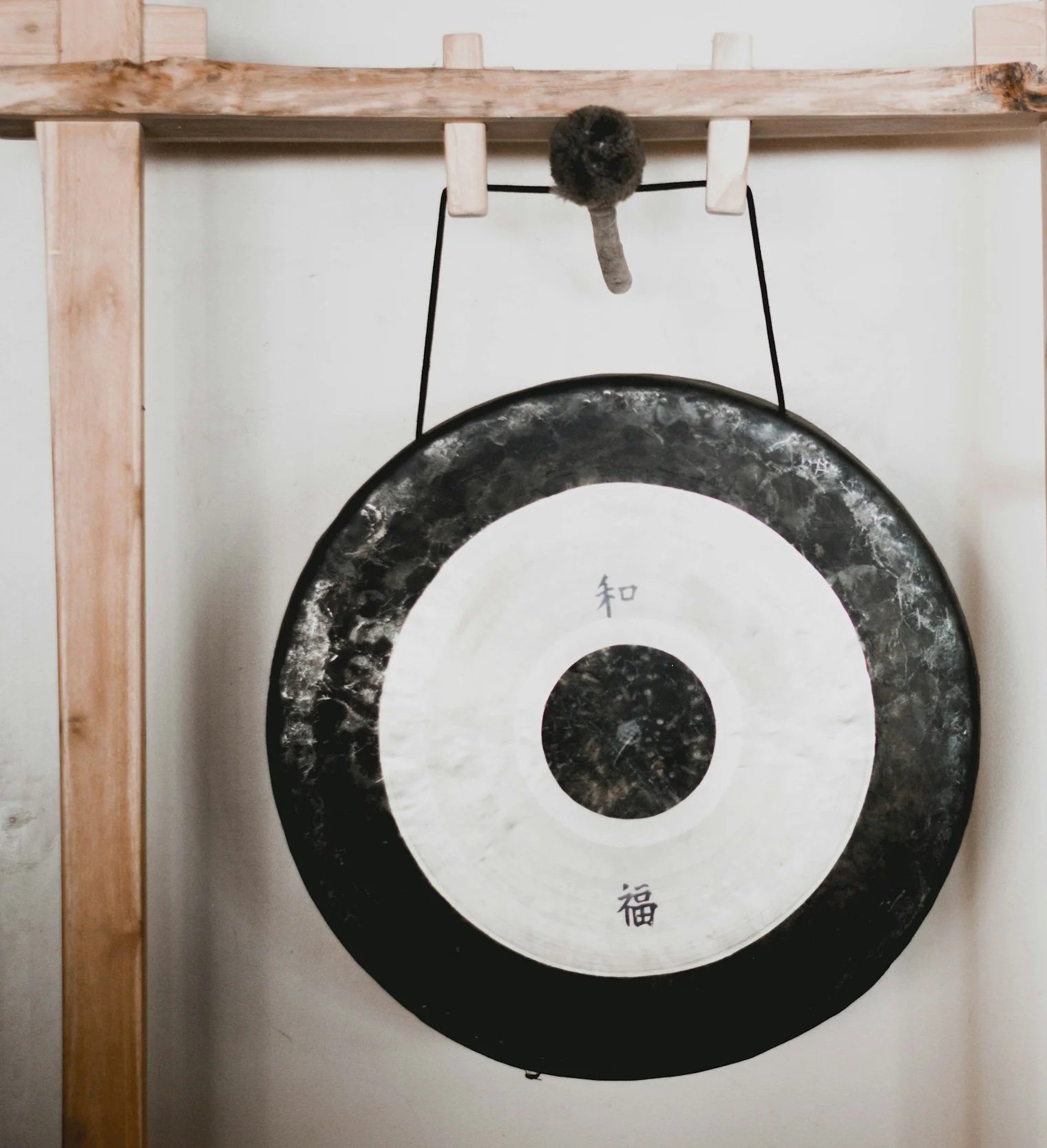 A gong with black and white concentric circles and Chinese characters hanging on a wooden stand for a group sound bath in Malaga