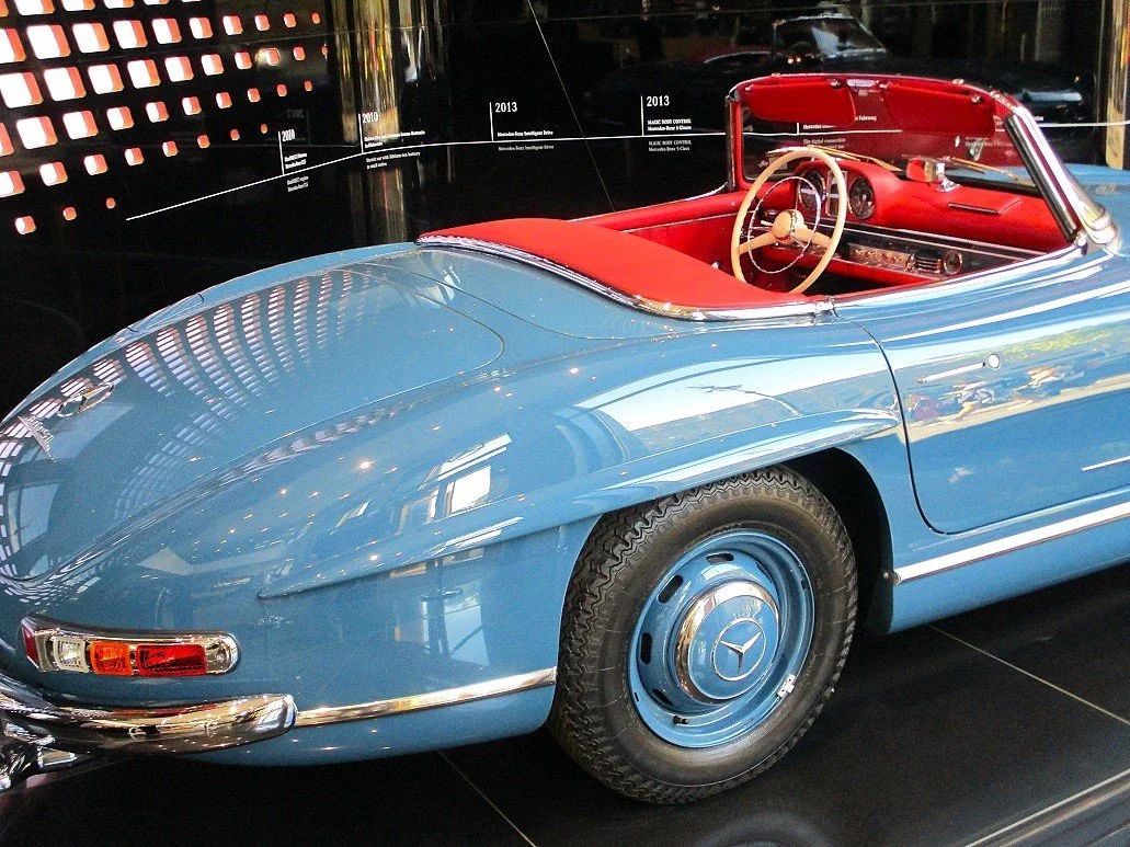 Heckpartie und den Innenraum eines blauen Mercedes-Benz 300 SL Roadster (Baureihe W 198 II) mit roter Leder-Innenausstattung und Verdeckabdeckung
