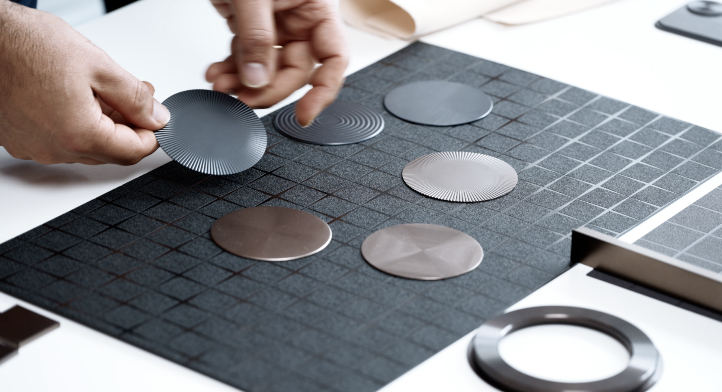 Person handling metallic color samples on a black grid display in a design or manufacturing setting.