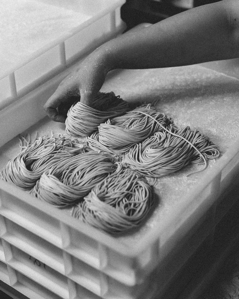 Hand beim Handrollen von rohem Teig zu Pasta auf einer ledigen Oberfläche