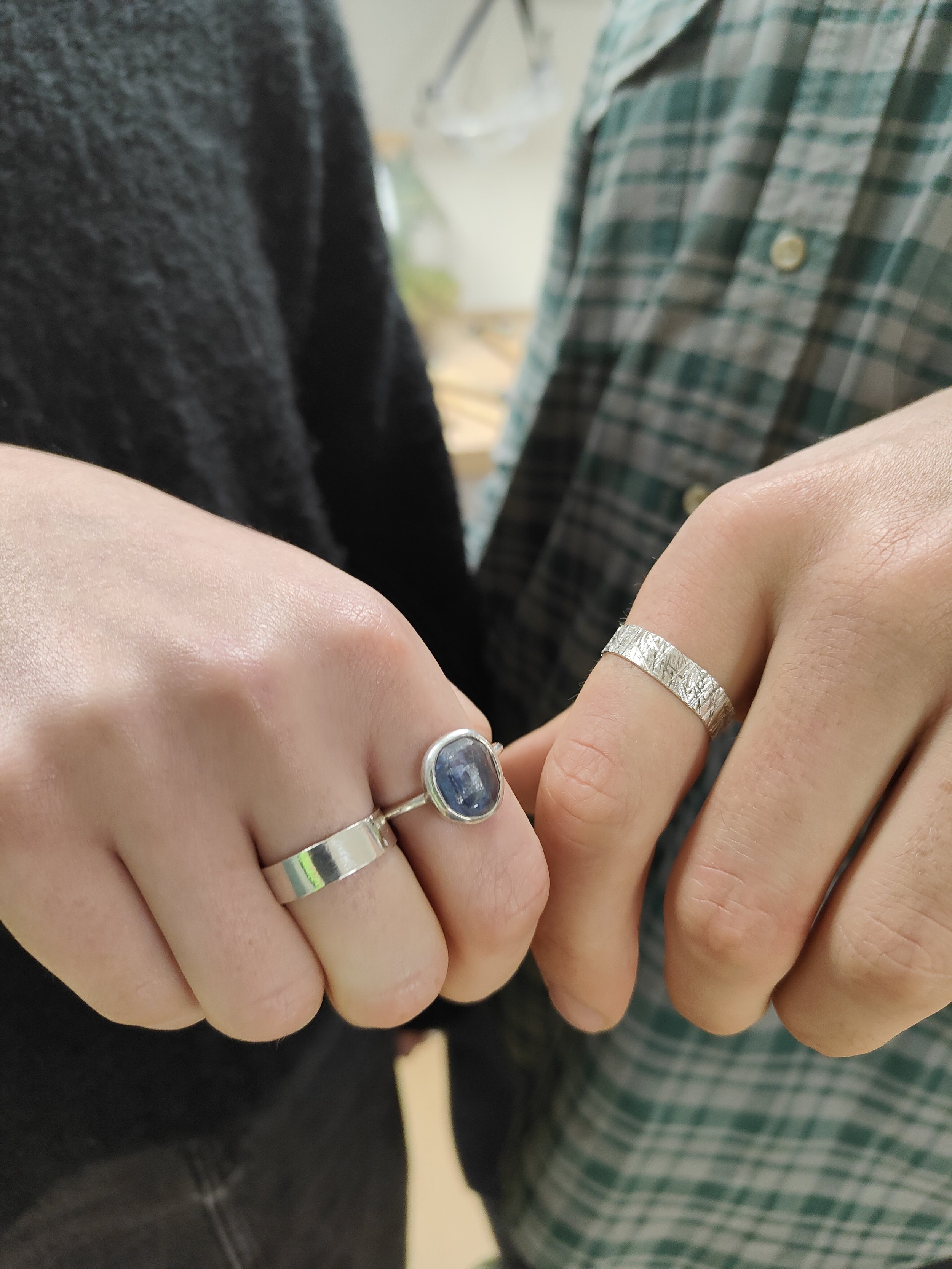 A pair of hands show handmade silver rings made in a beginners ring making workshop at Silver & Steel. One silver ring has a mirror finish and one has texture.