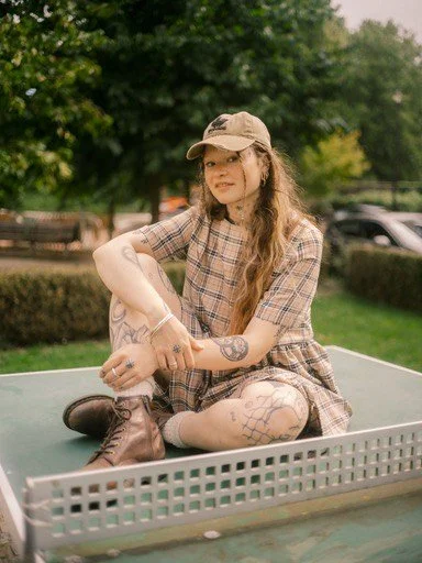 Young woman with tattoos looking confidently at the camera dressed in reworked burberry