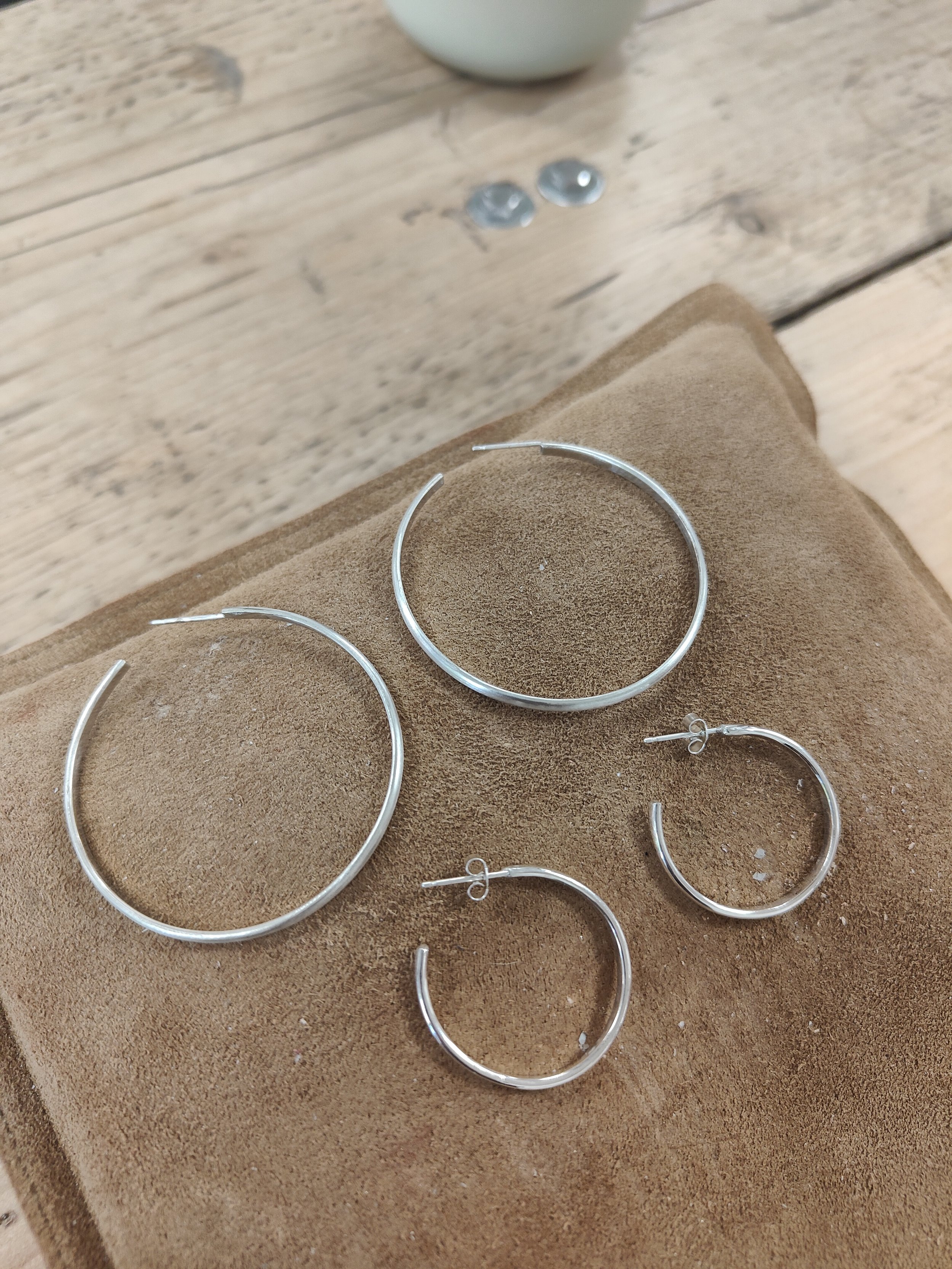 Two pairs of handmade silver hoops sat on brown sandbag on workshop table