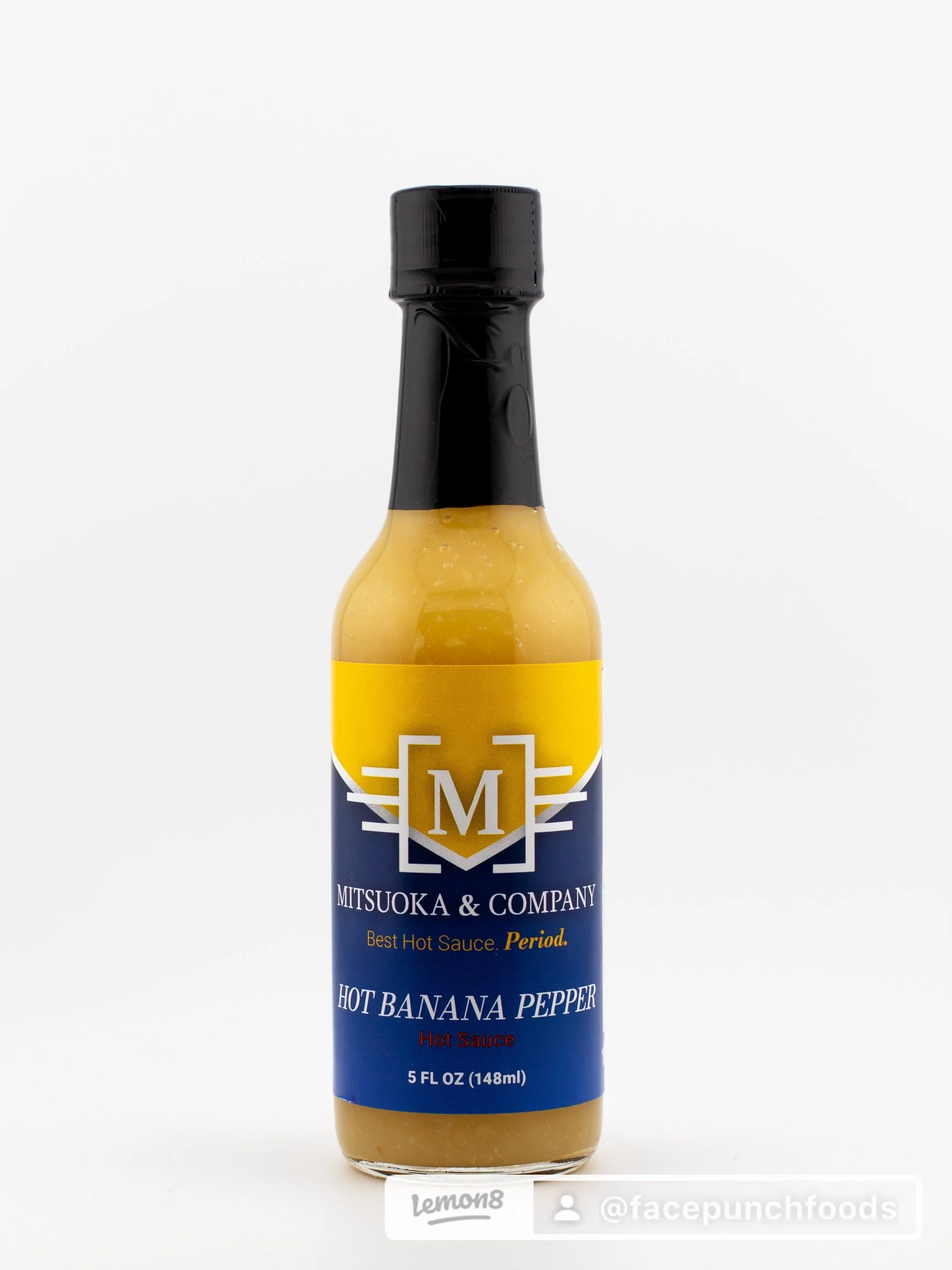 Bottle of hot banana pepper hot sauce for Mitsuoka & Company with a yellow and blue label and black cap.