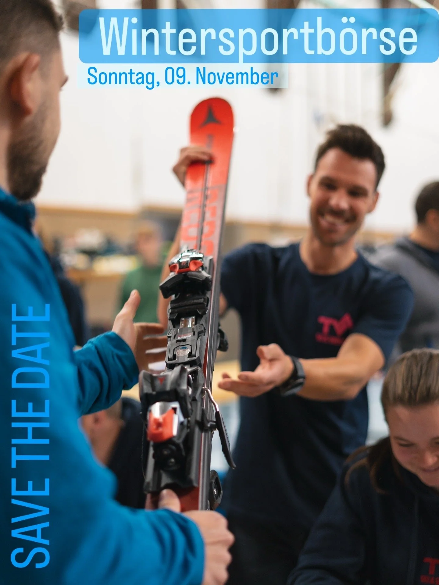 Drei Menschen beim Austausch eines Skis in einer Gruppe, im Hintergrund mehrere weitere Personen, vermutlich bei einer Wintersport-Event.