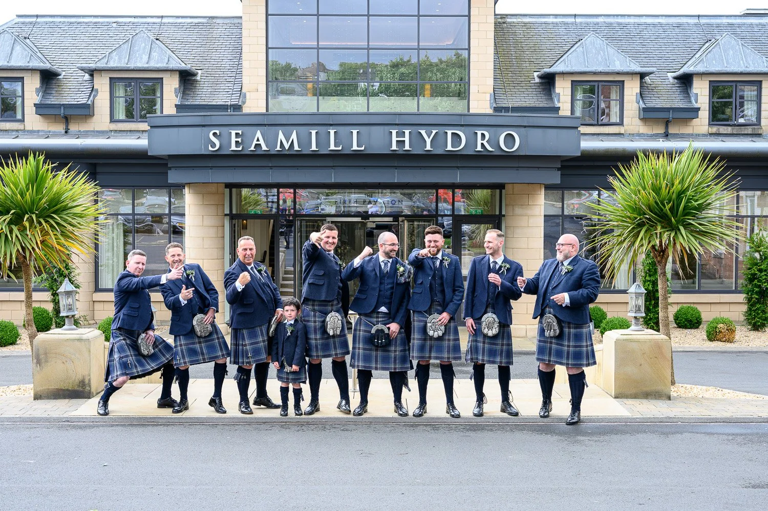 Groomsmen having fun and pointing at the camera outside the main entrance of Seamill Hydro Hotel.