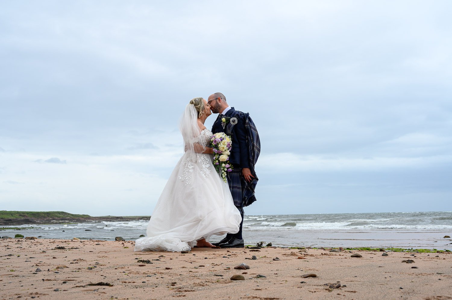 A romantic photo of a bride and groom kissing on the beach at Seamill Hydro with the sea in the background.
