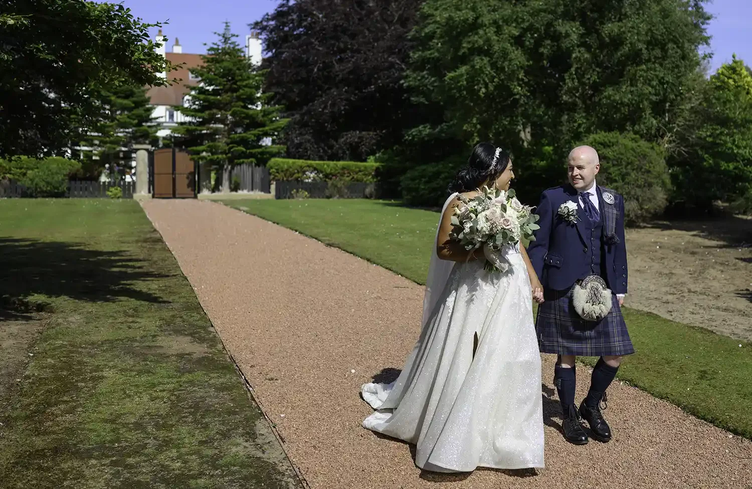 Bride and groom walking together along the red gravel garden path at Lochgreen House Hotel wedding venue in Troon Ayrshire