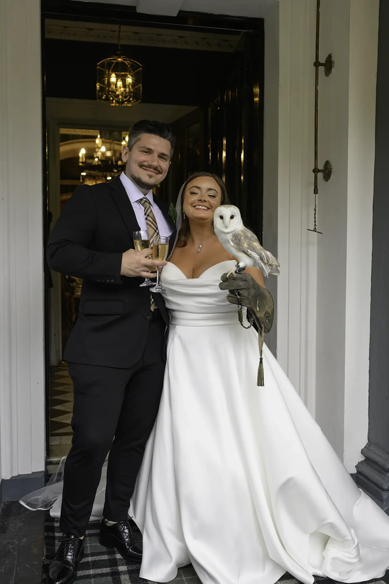 Bride and groom holding champagne with owl at Auchen Castle in Moffat