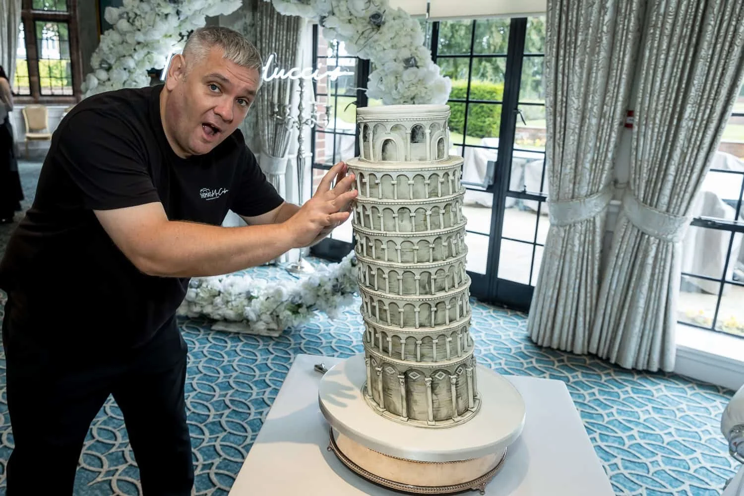 Thomas playfully posing as if holding up a Leaning Tower of Pisa wedding cake, showcasing his sense of humor and love for baking.