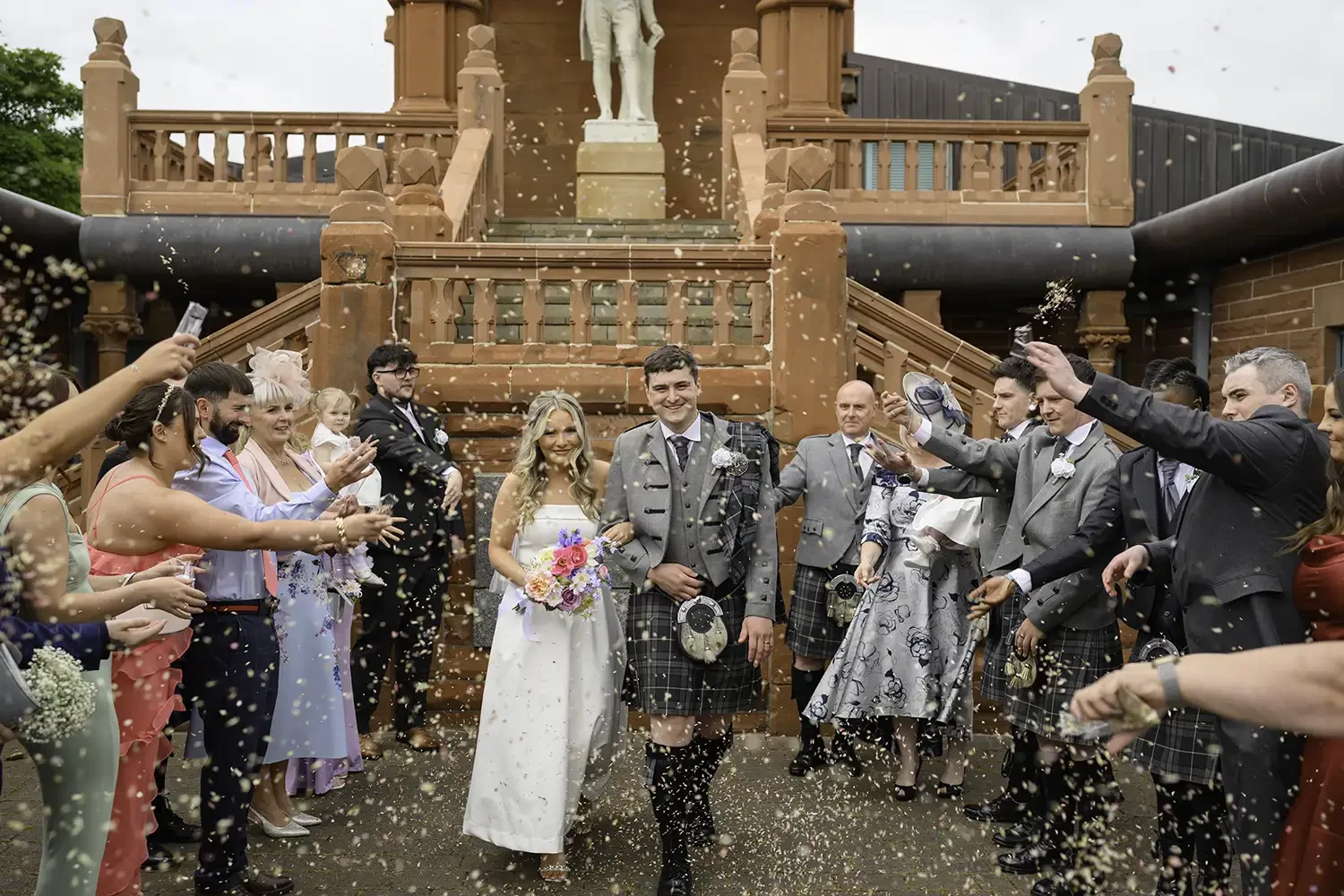 Aaron and Linzi walking through confetti outside Burns Monument in Kilmarnock after their wedding ceremony.