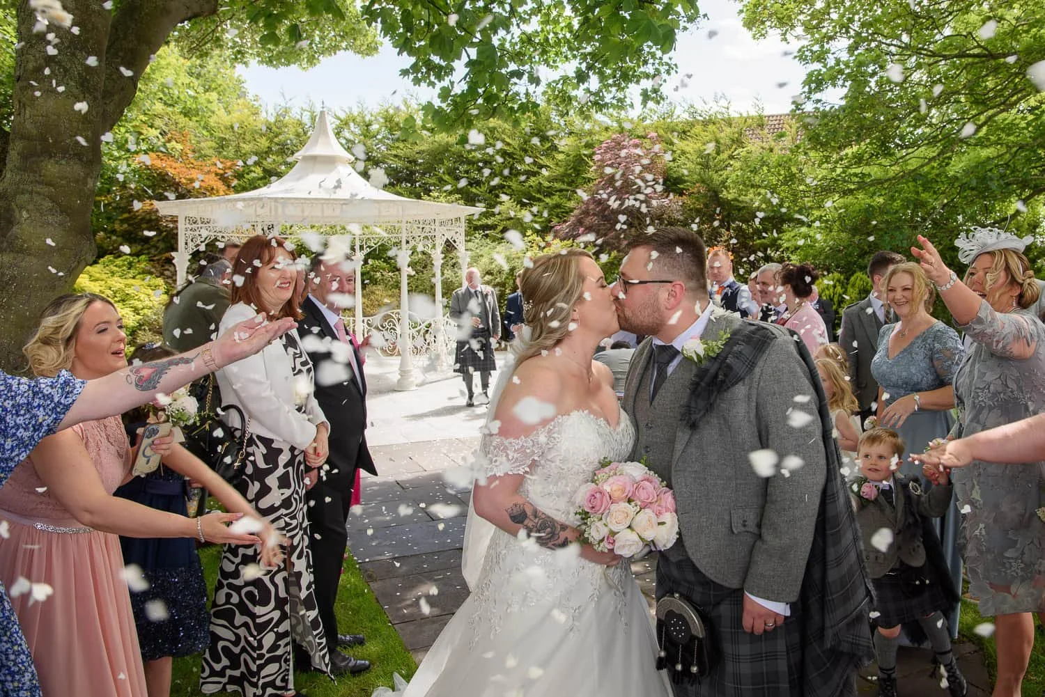 Bride and groom kissing during confetti throw outside gazebo at The Carlton Hotel Prestwick