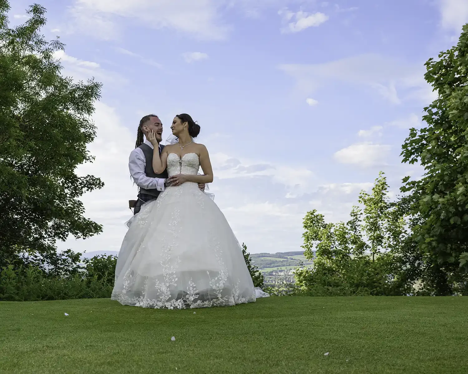 Bride and groom embracing on lawn at Gleddoch House Hotel in Langbank with scenic views