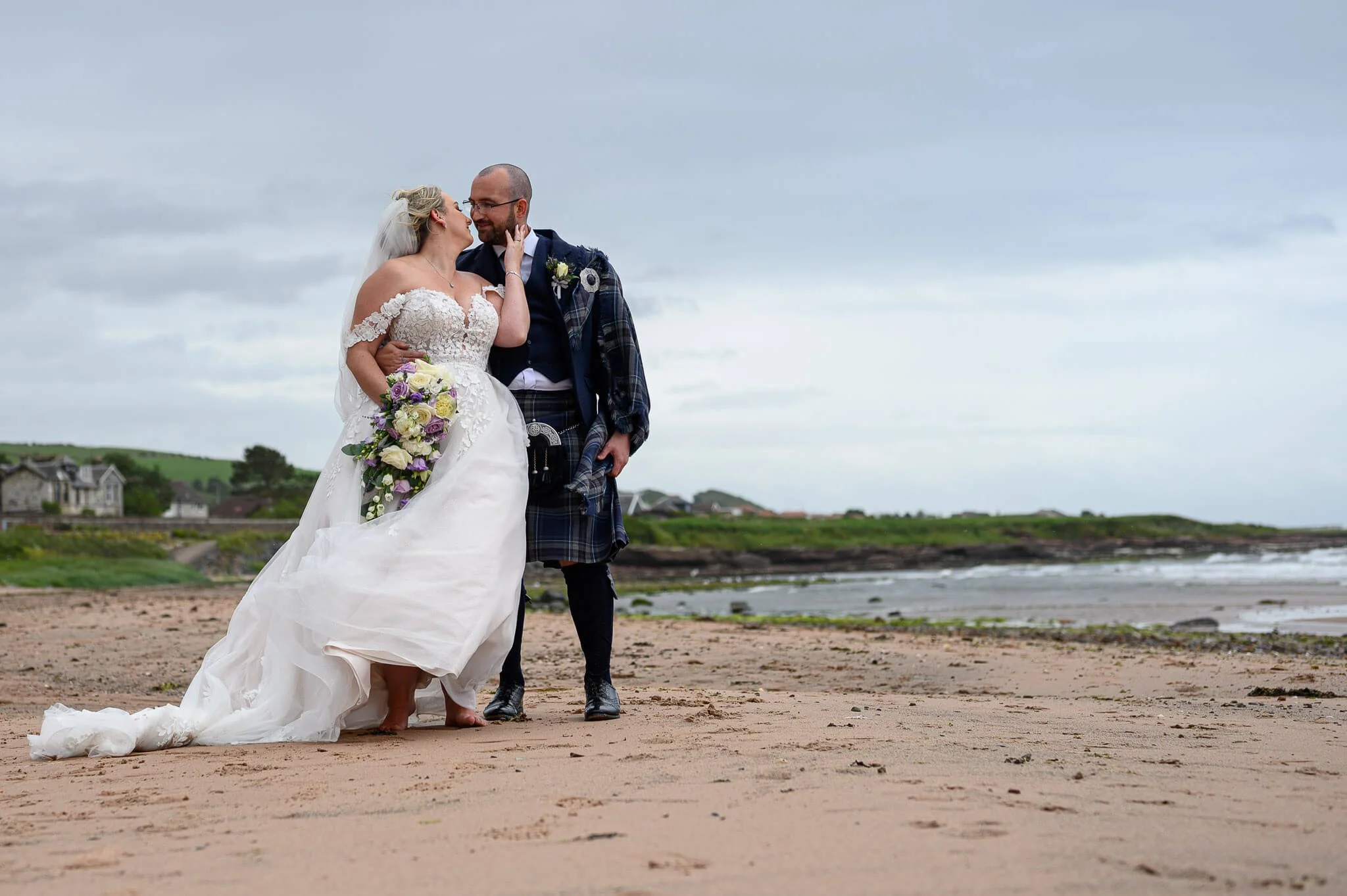 A happy bride and groom sharing a quiet, comfortable moment on the beach behind the Seamill Hydro Hotel, showcasing the relaxed and fun wedding photography style of Thomas McCabe