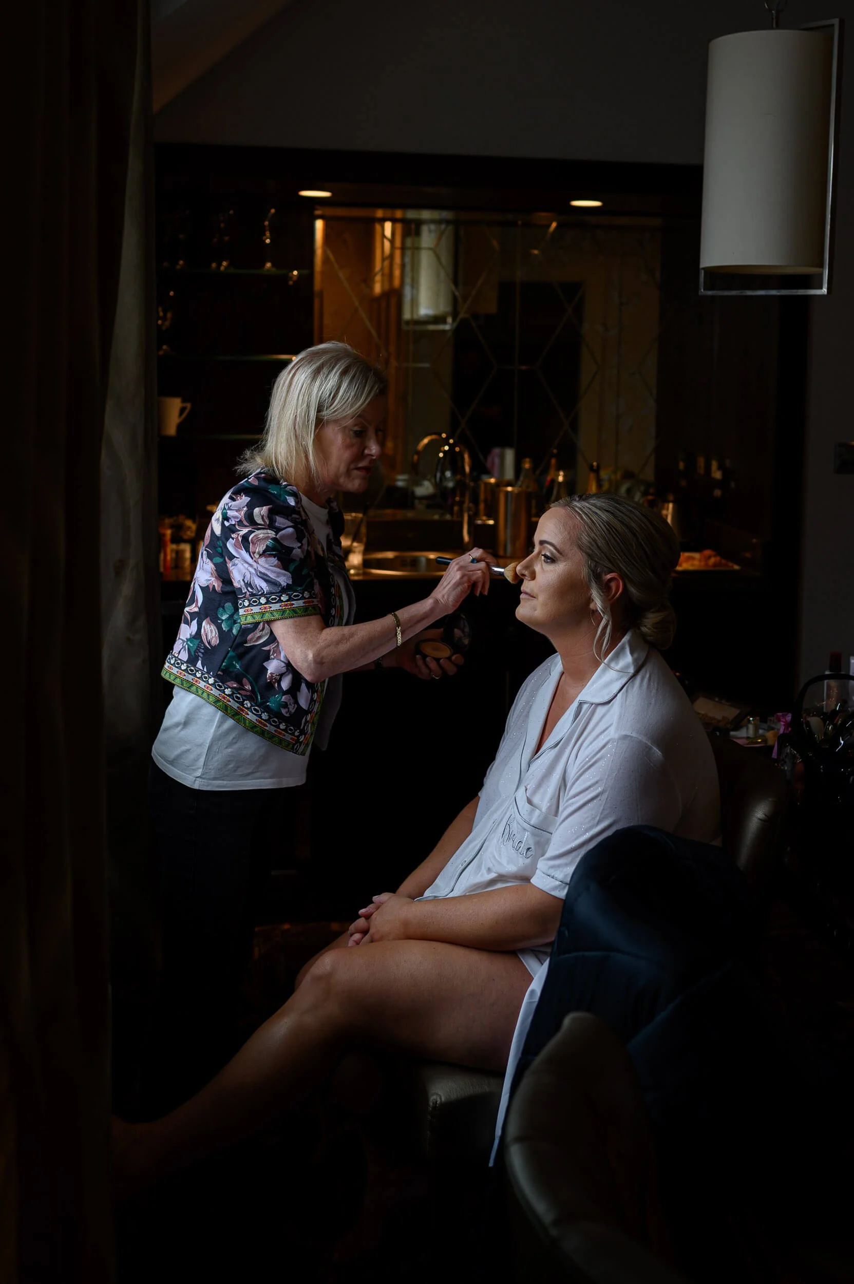 Bride getting ready at Seamill Hydro as soft natural window light falls across her face during makeup preparation. The intimate moment captures the calm before the ceremony, with warm tones and gentle shadows creating a timeless, elegant atmosphere.