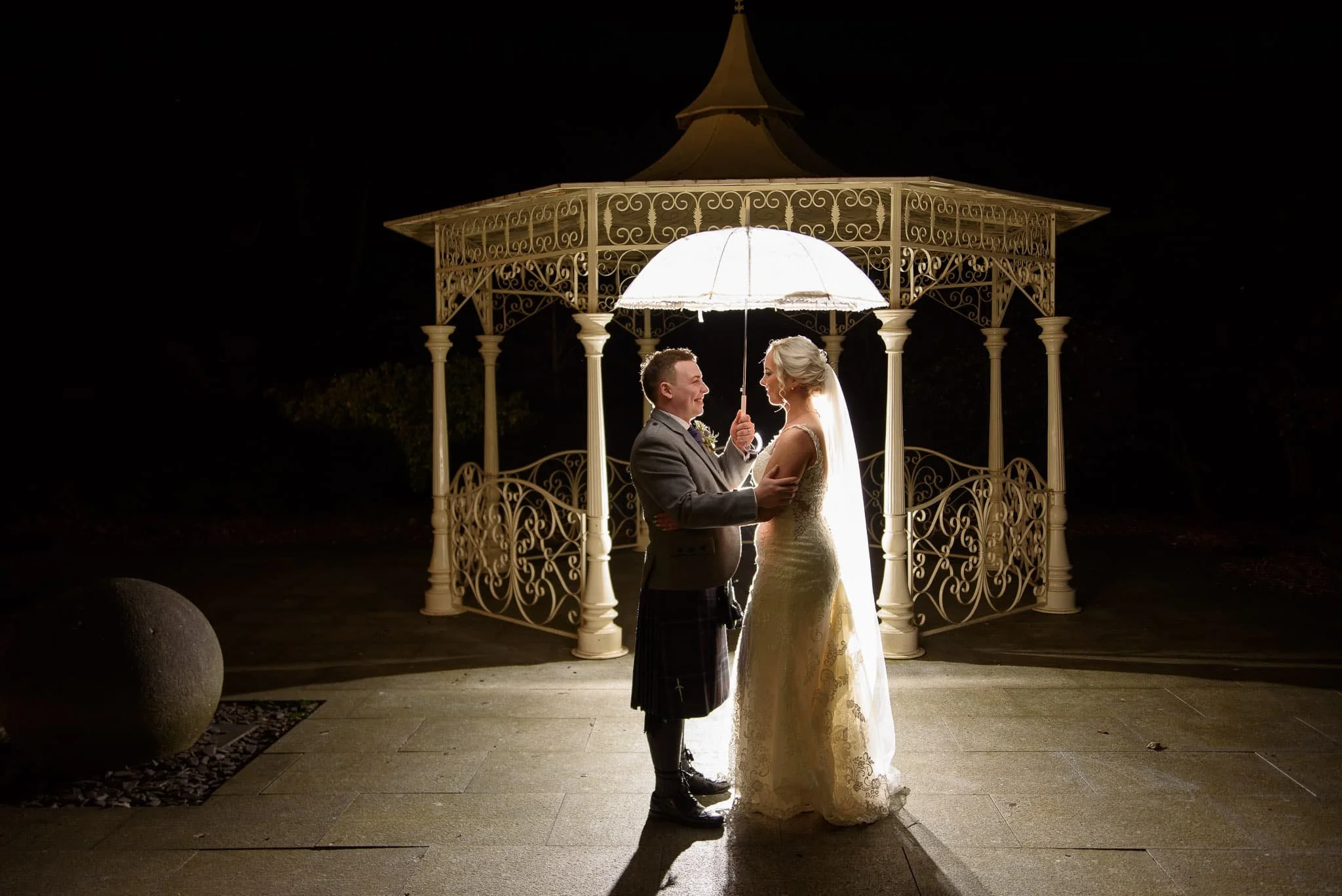 Bride and groom under illuminated gazebo at The Carlton Hotel in Prestwick during evening wedding portraits.