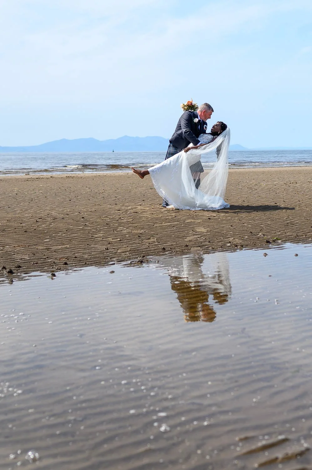 A romantic beach portrait in Ayrshire as the groom lifts his bride against the soft tones of the sea and sky. A timeless seaside wedding moment captured in a natural and relaxed style.