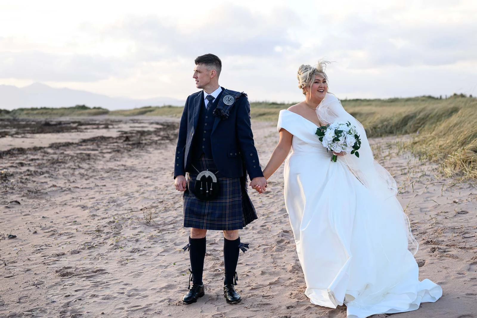 A relaxed bride and groom walking along the stunning Ayrshire coastline, captured by a natural wedding photographer.