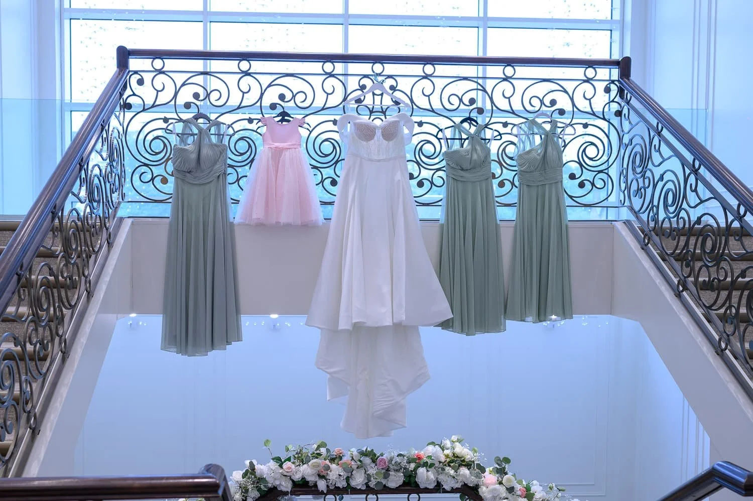 Bride’s wedding dress displayed on the staircase at Seamill Hydro Hotel alongside bridesmaid dresses and a pink flower girl dress in West Kilbride.
