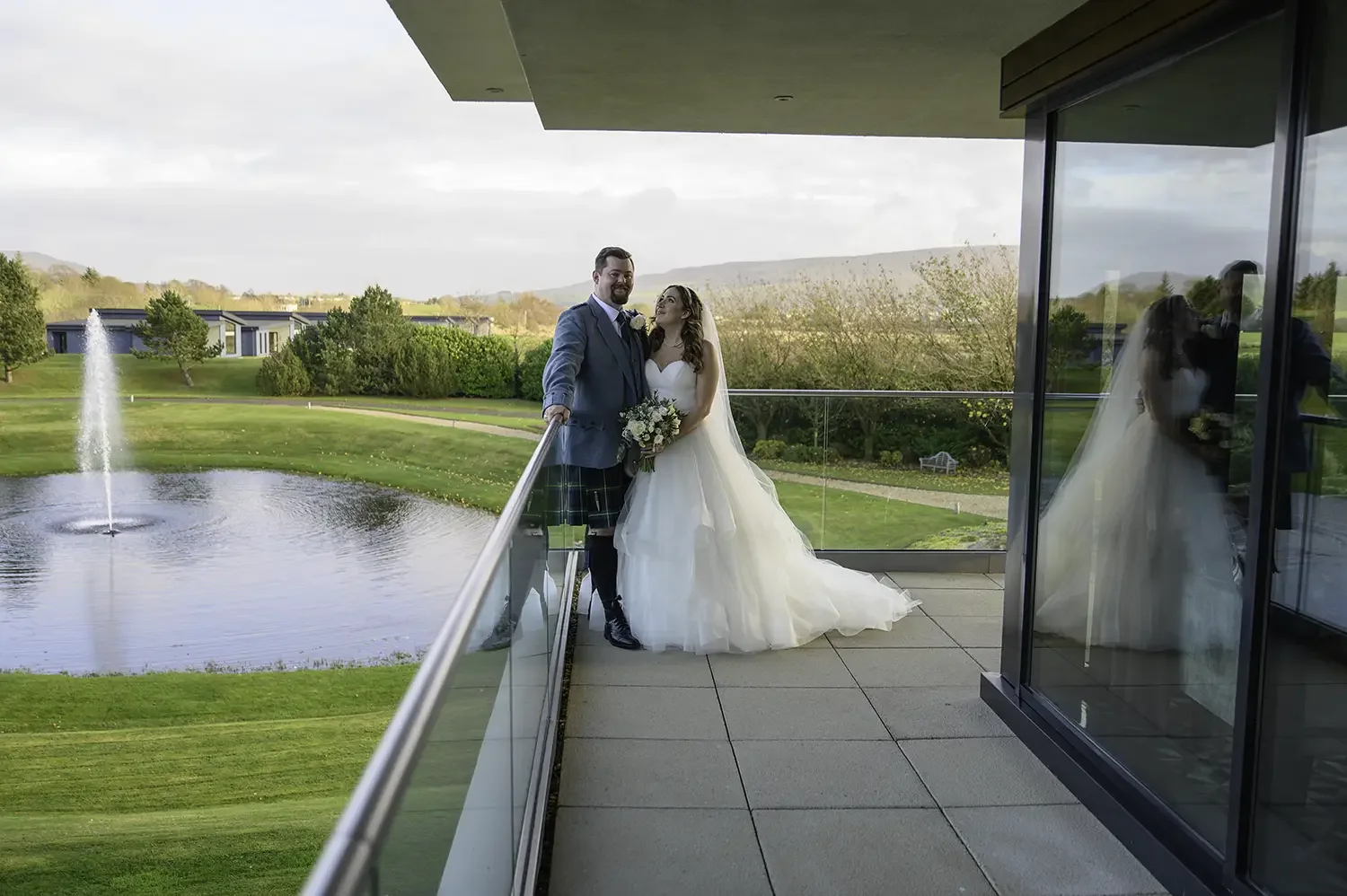Bride and groom on balcony overlooking pond at Lochside House Hotel in New Cumnock