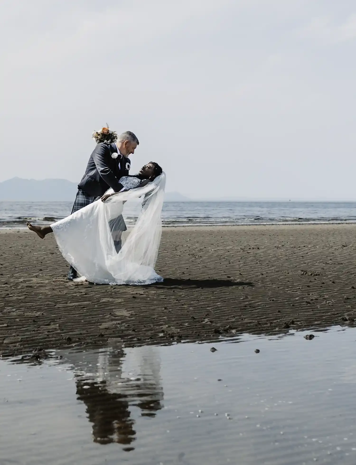 Bride and groom on Ayr beach with veil flowing and sea view