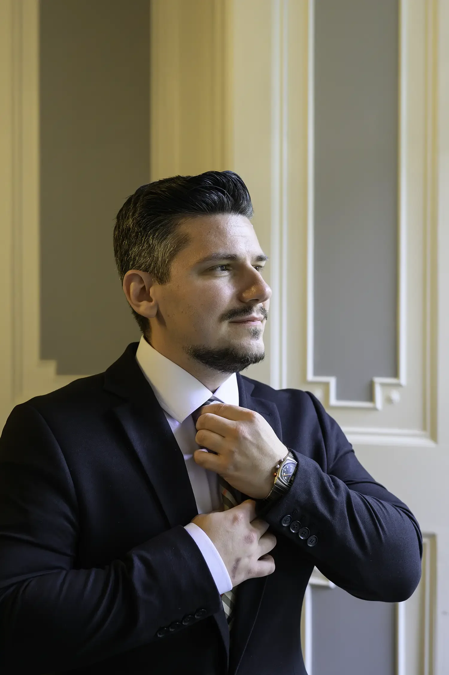 Groom adjusting his tie by window light at Auchen Castle wedding venue in Moffat