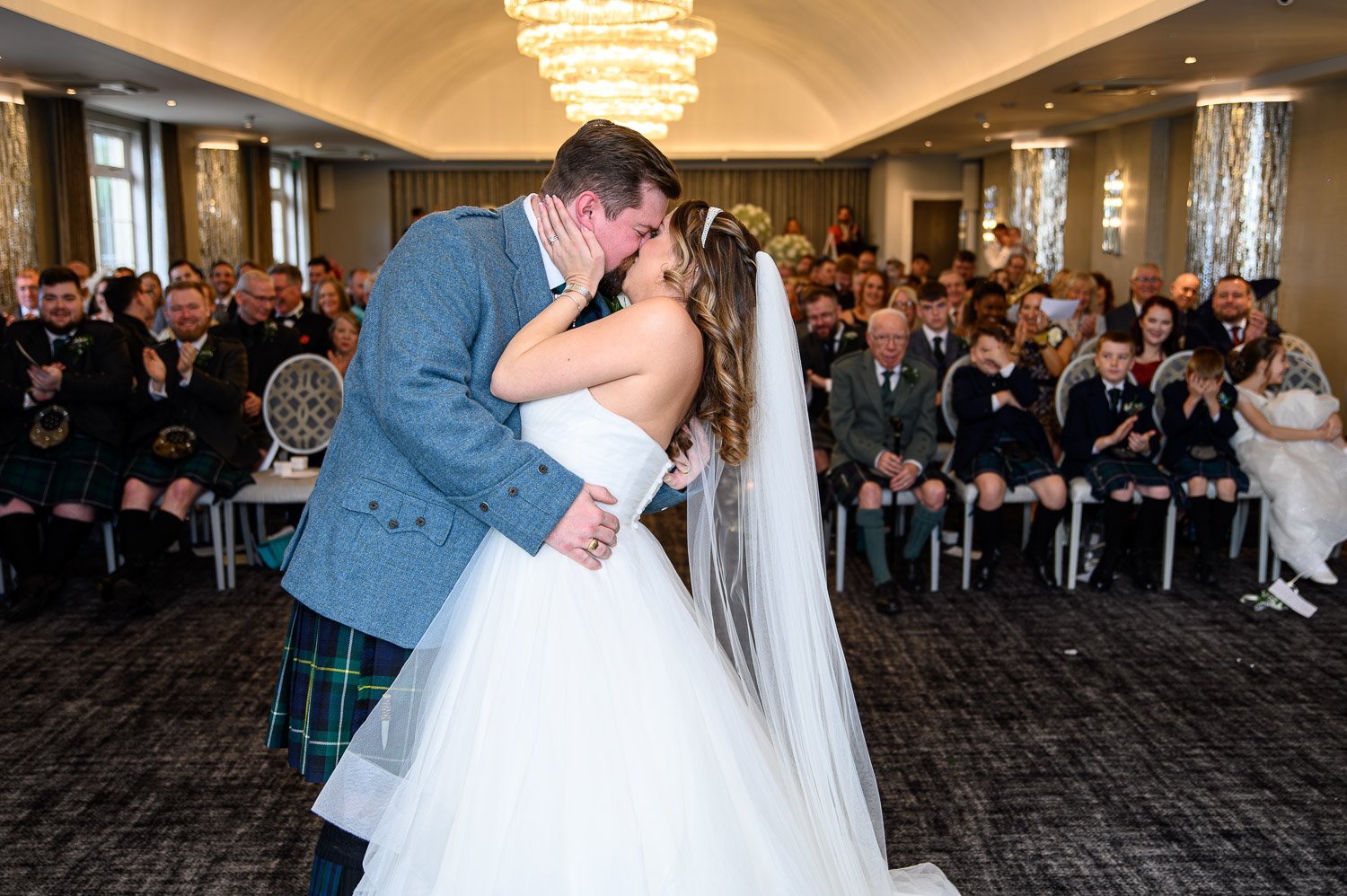 A bride and groom sharing their first kiss during an indoor ceremony at Lochside House Hotel.