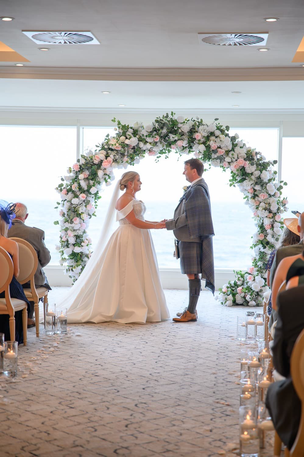 Bride and groom during their wedding ceremony under a floral arch at Seamill Hydro Hotel.