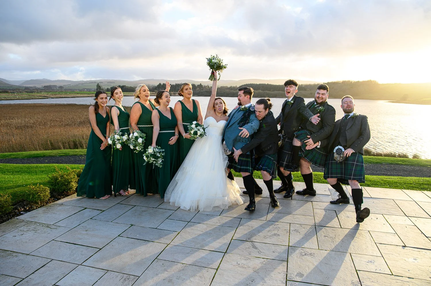 A large, cheering bridal party celebrating on the terrace at Lochside House Hotel during sunset.