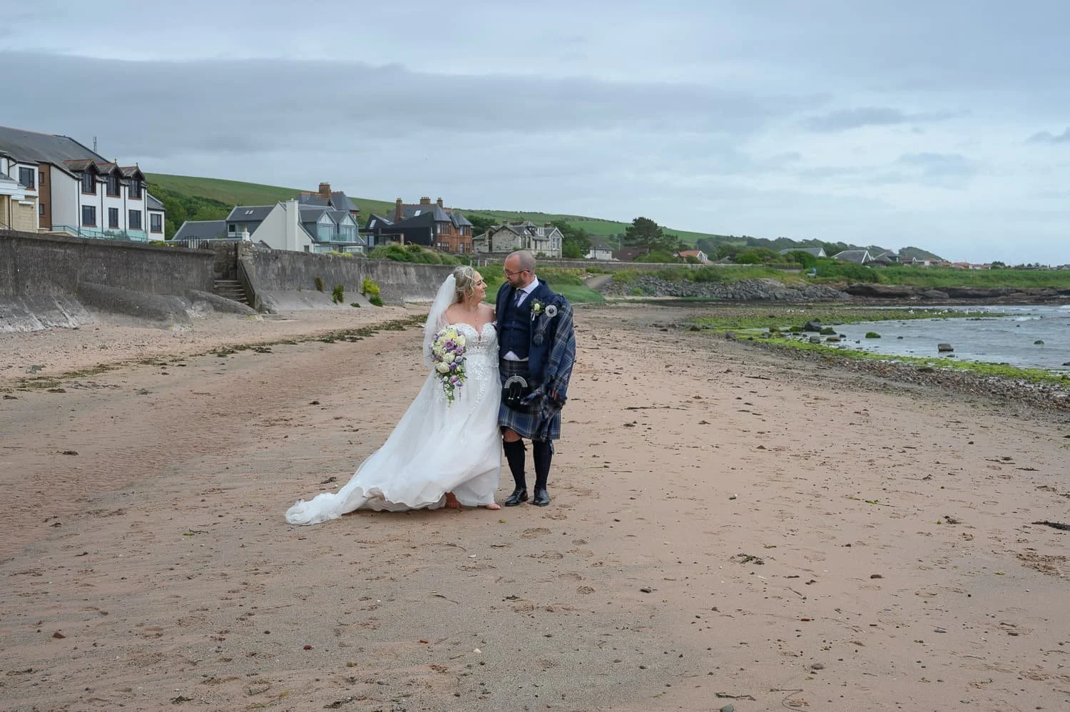 Bride and groom walking along the beach at Seamill Hydro Hotel in West Kilbride during their wedding day.