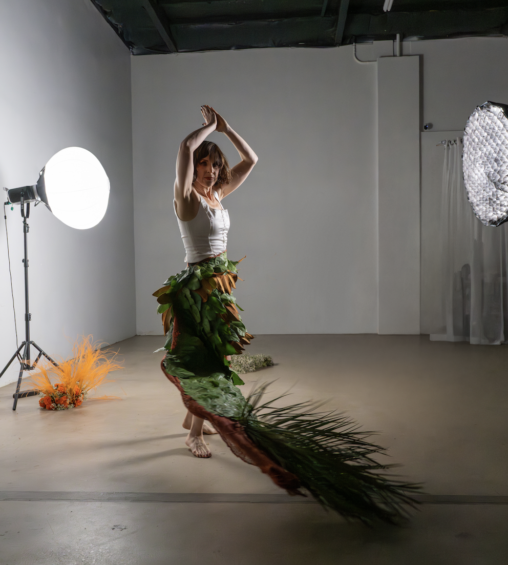 A woman in a costume made of leaves dancing in a studio with studio lighting equipment.