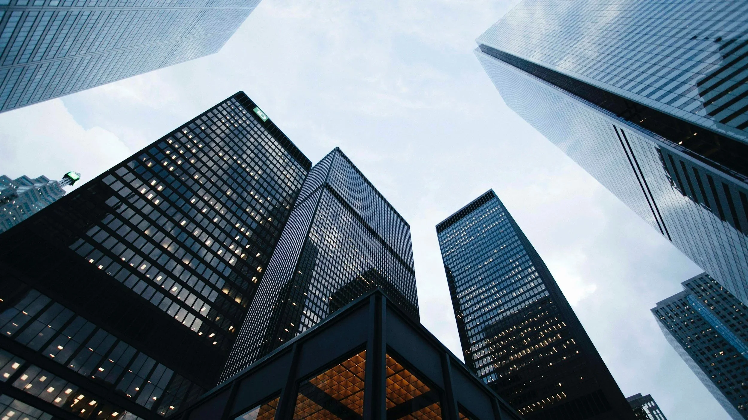 Low-angle view of modern glass skyscrapers in a city during daytime, with a pale sky in the background.