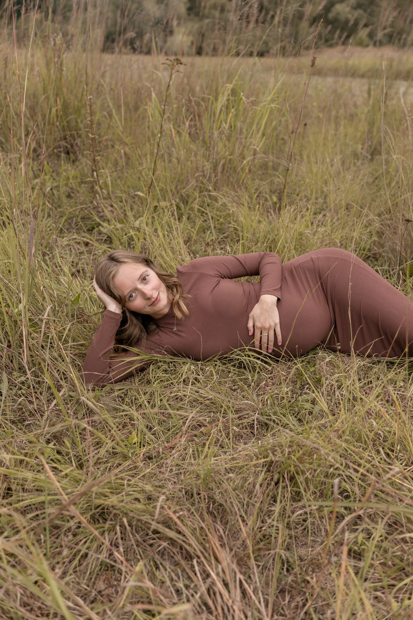A woman holding a newborn baby, with her head tilted towards a man sitting nearby, in a cozy indoor setting with a brick wall background. Photo by Feinauer Photography in Bay City, Michigan studio space.