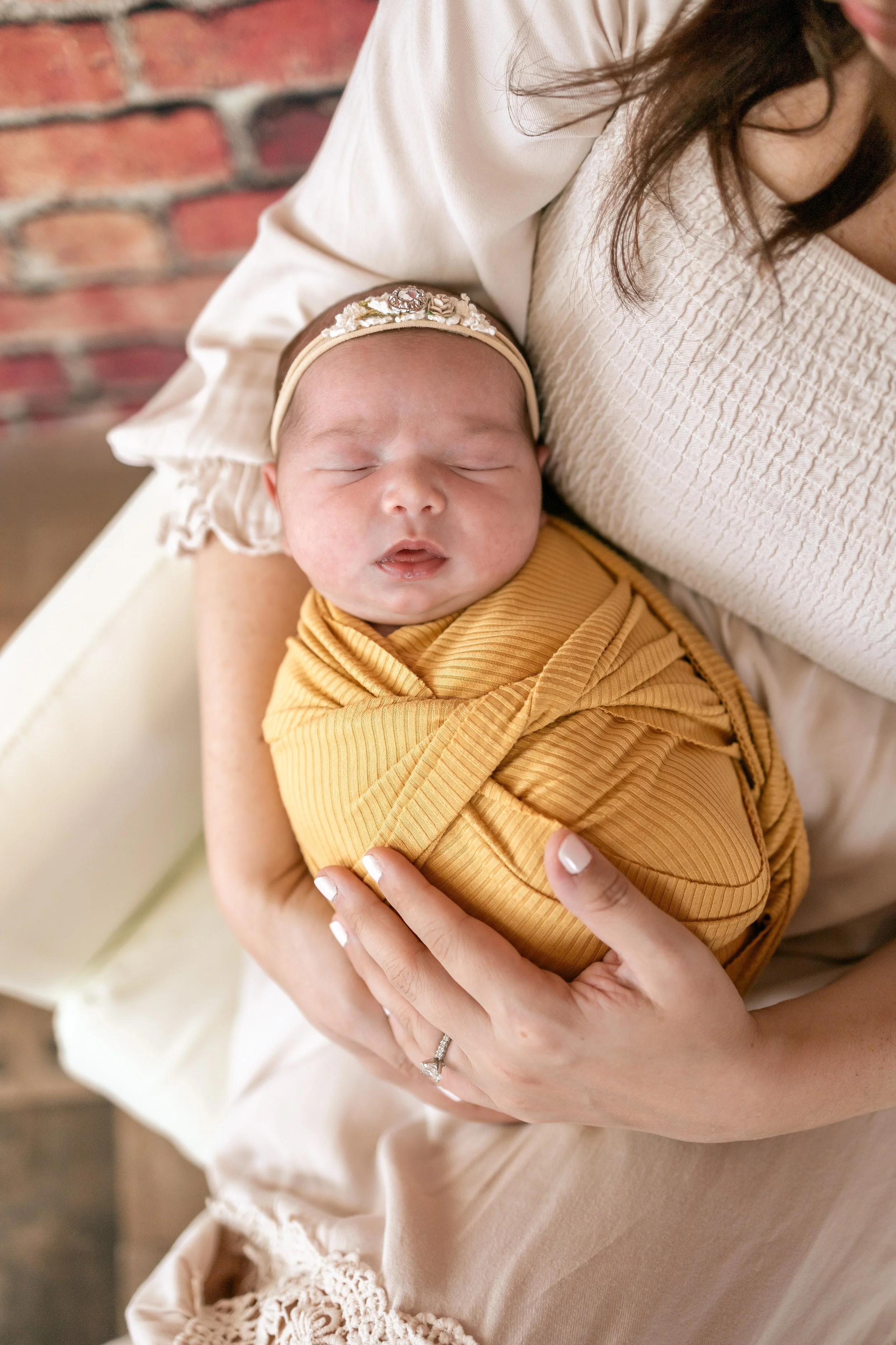 A baby wrapped in a mustard yellow blanket, sleeping peacefully in a woman's arms.