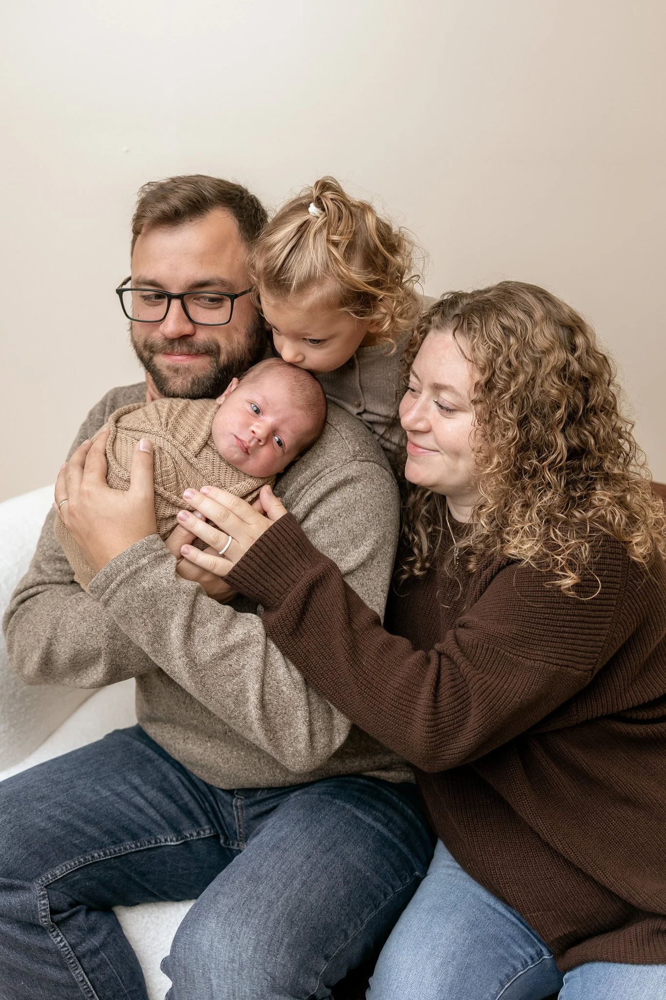 Family portrait of parents and young daughter cuddling a newborn baby at home