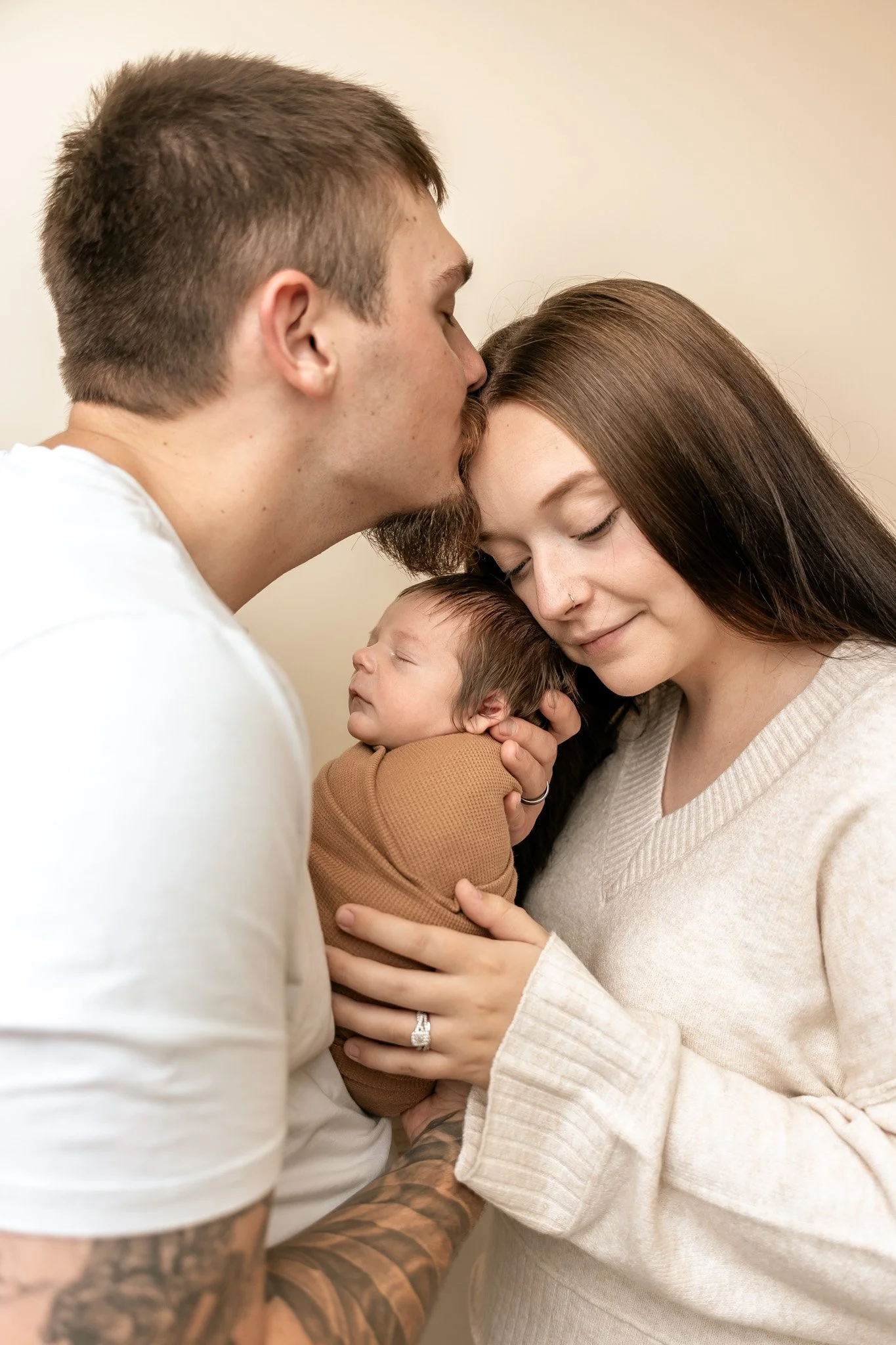 Parents lovingly hold and kiss their sleeping newborn baby at home.
