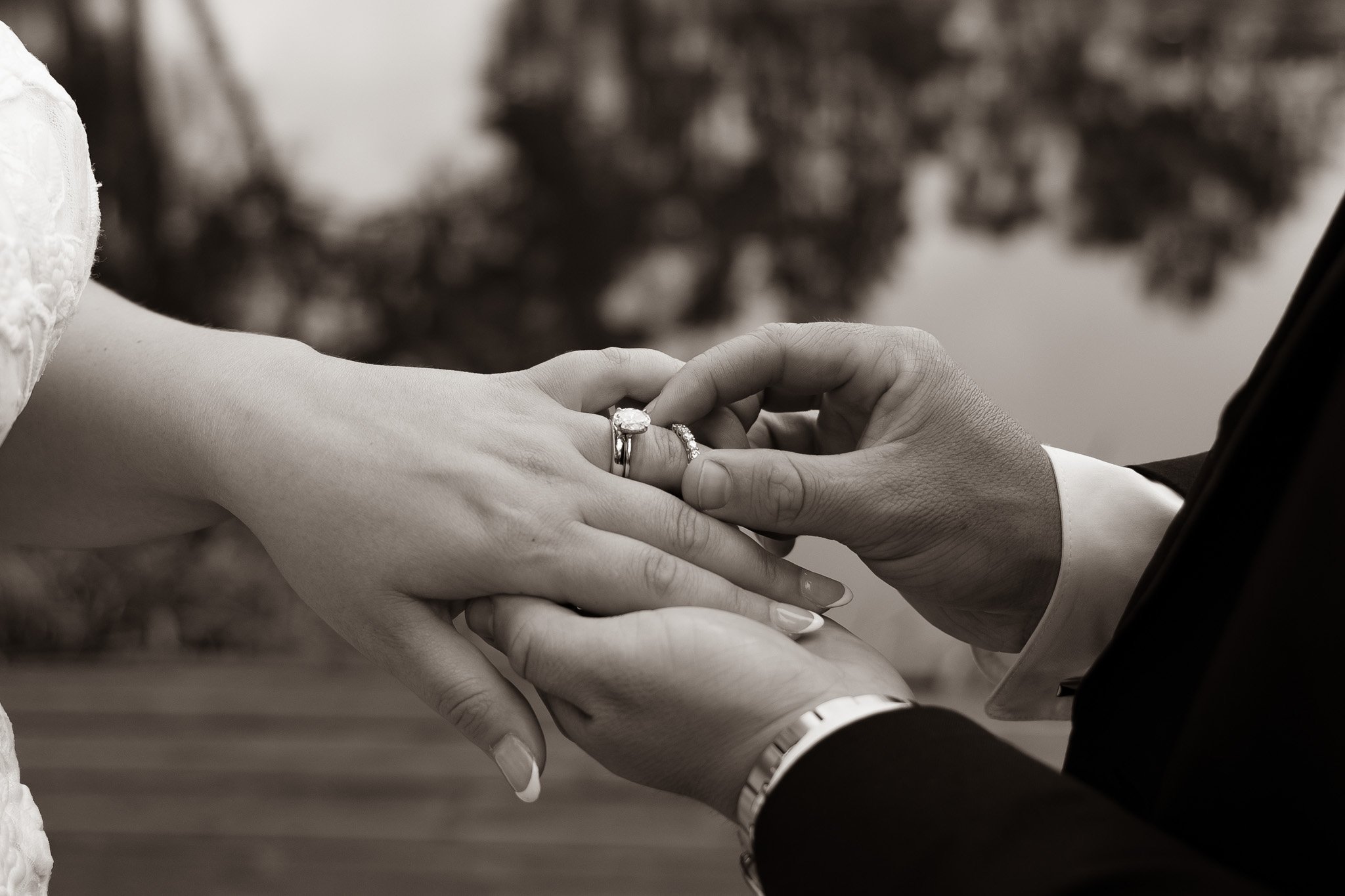 Close-up of a man and woman holding hands with wedding rings, in black and white, during a wedding ceremony.