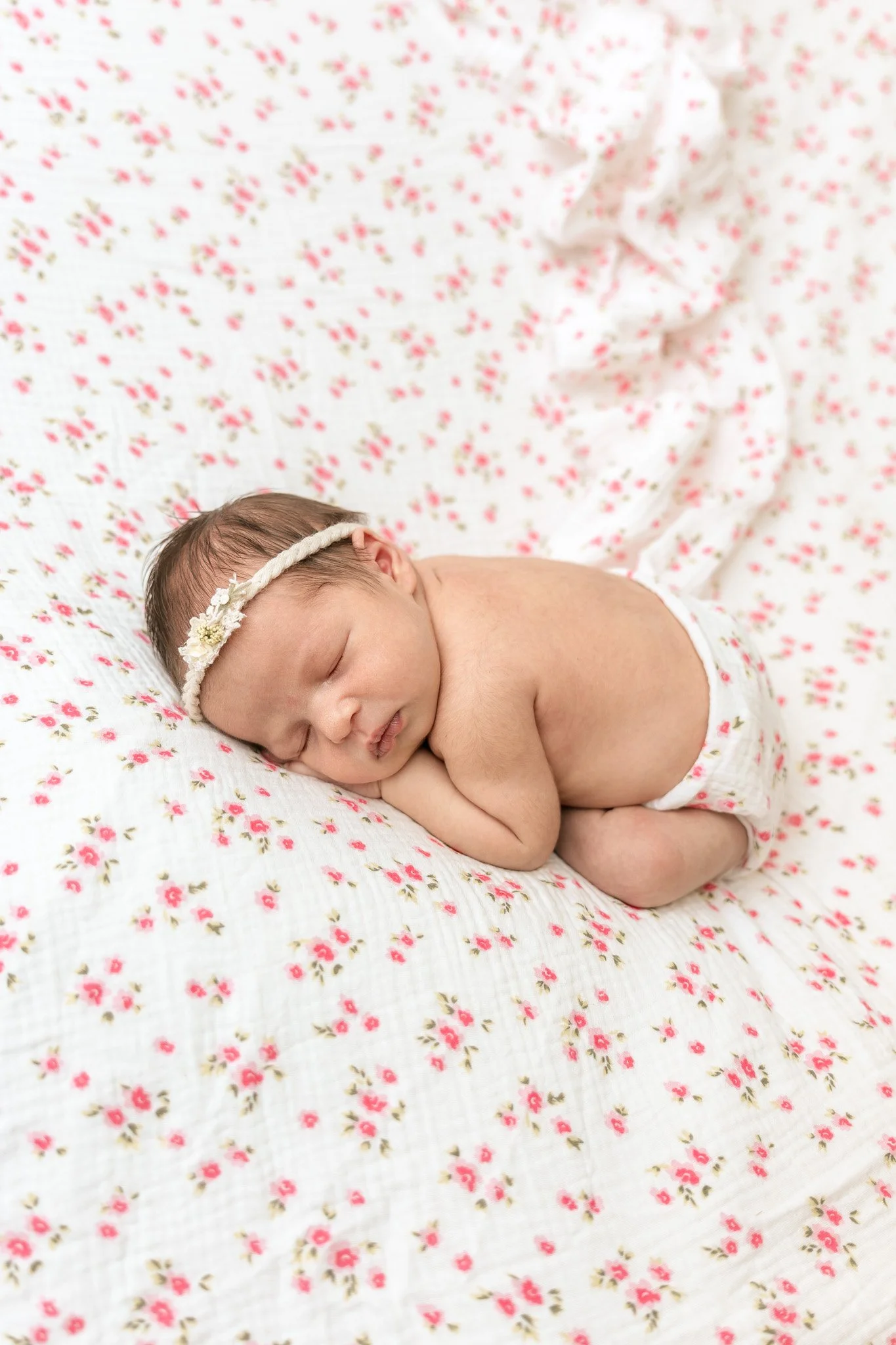 Sleeping newborn baby wearing a floral headband on a pink-and-white floral blanket