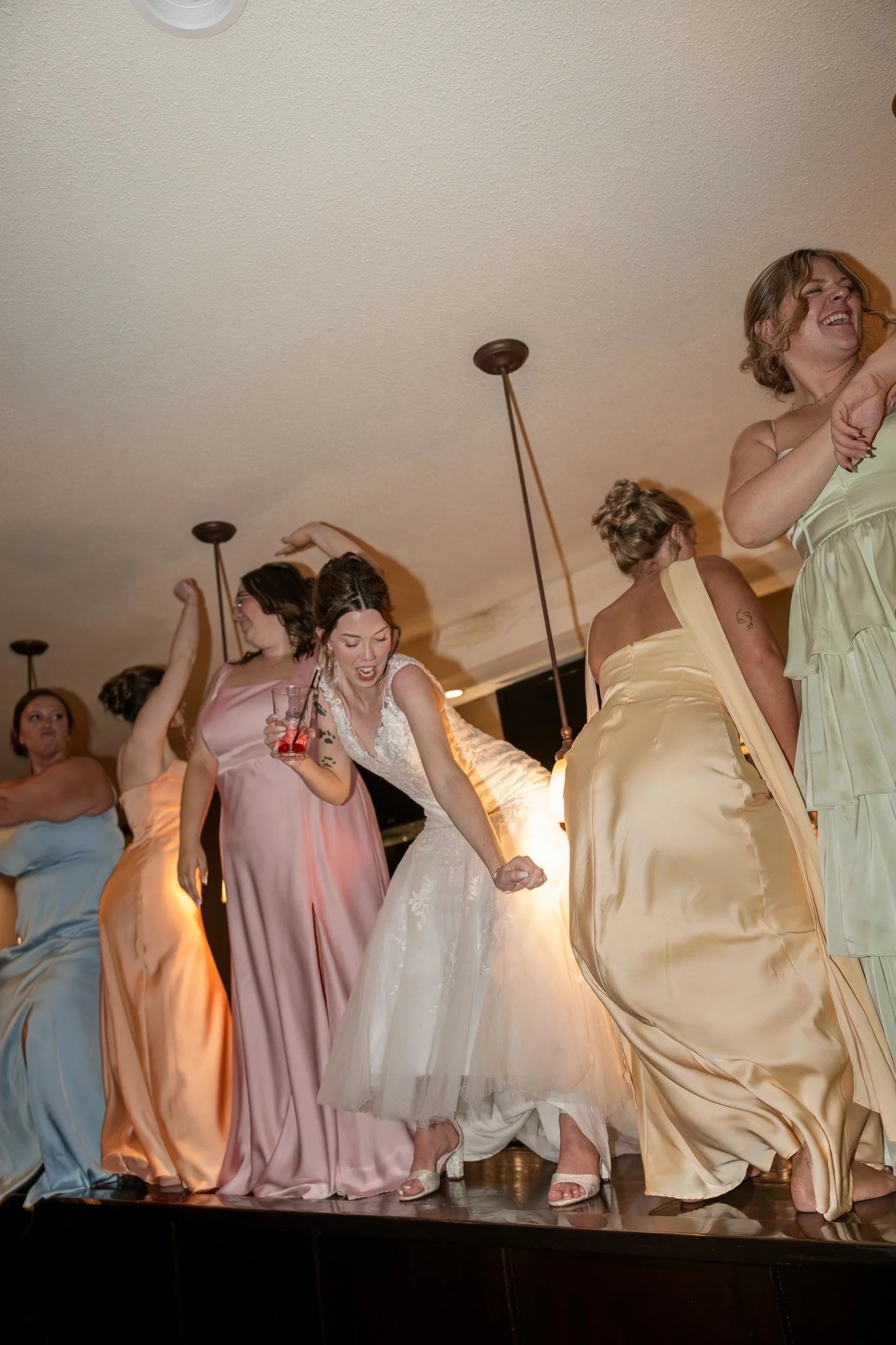 Bridesmaids in colorful dresses dancing and celebrating at a wedding reception.
