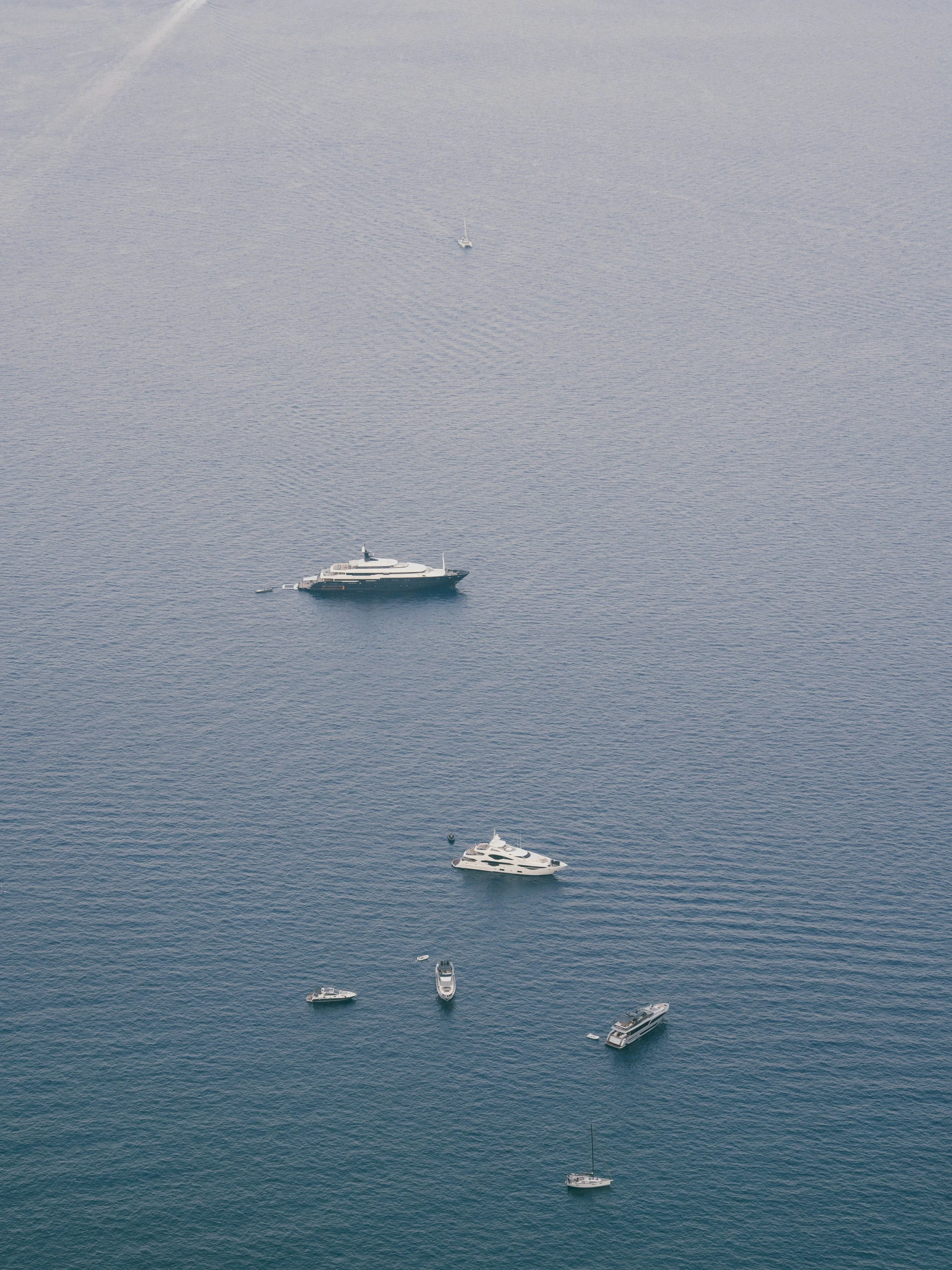 Several yachts and boats are anchored in a calm, open body of water with a uniform blue-gray color.