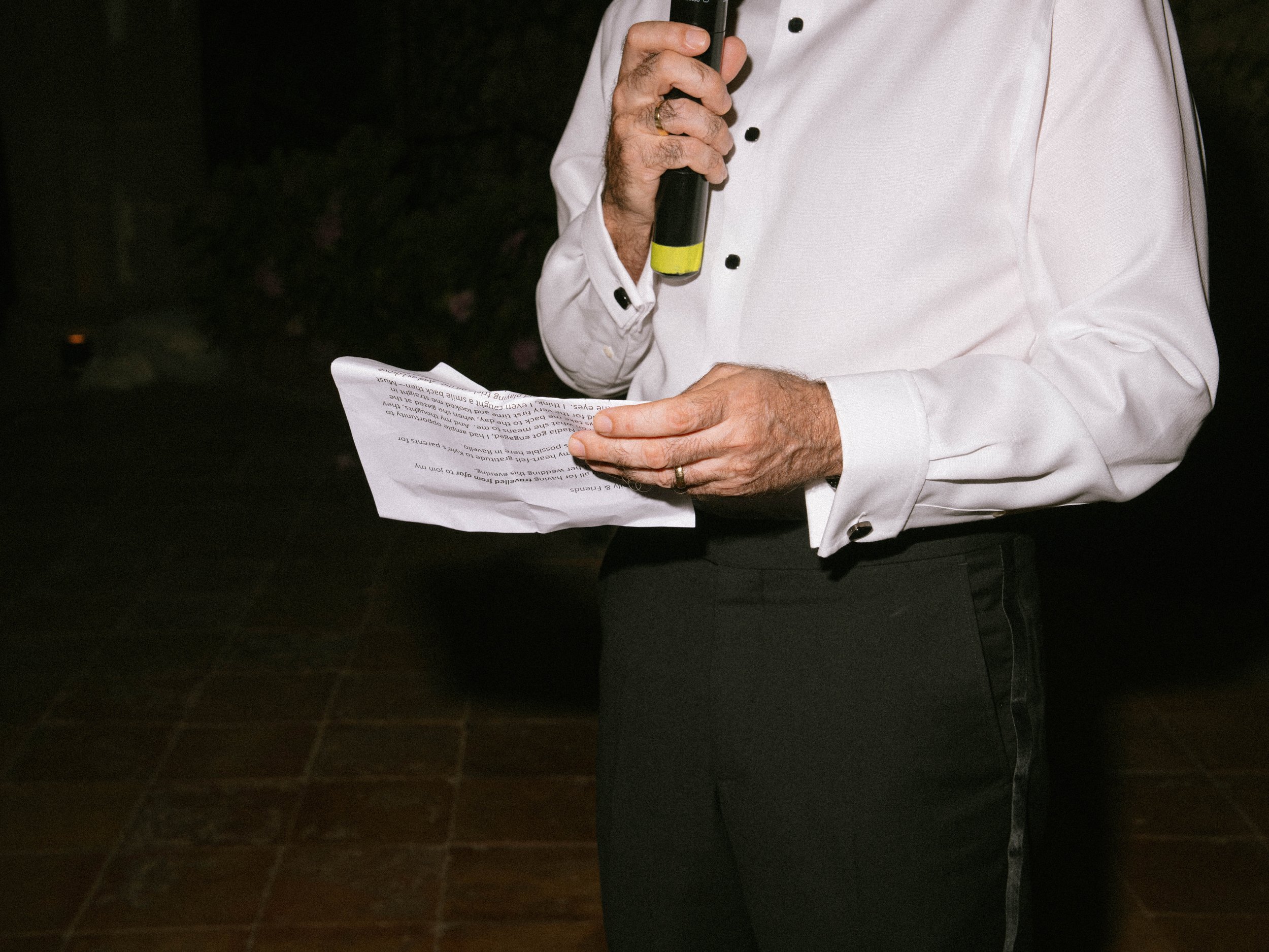 A person wearing a white shirt holding a piece of paper in front of their body in a dark environment.