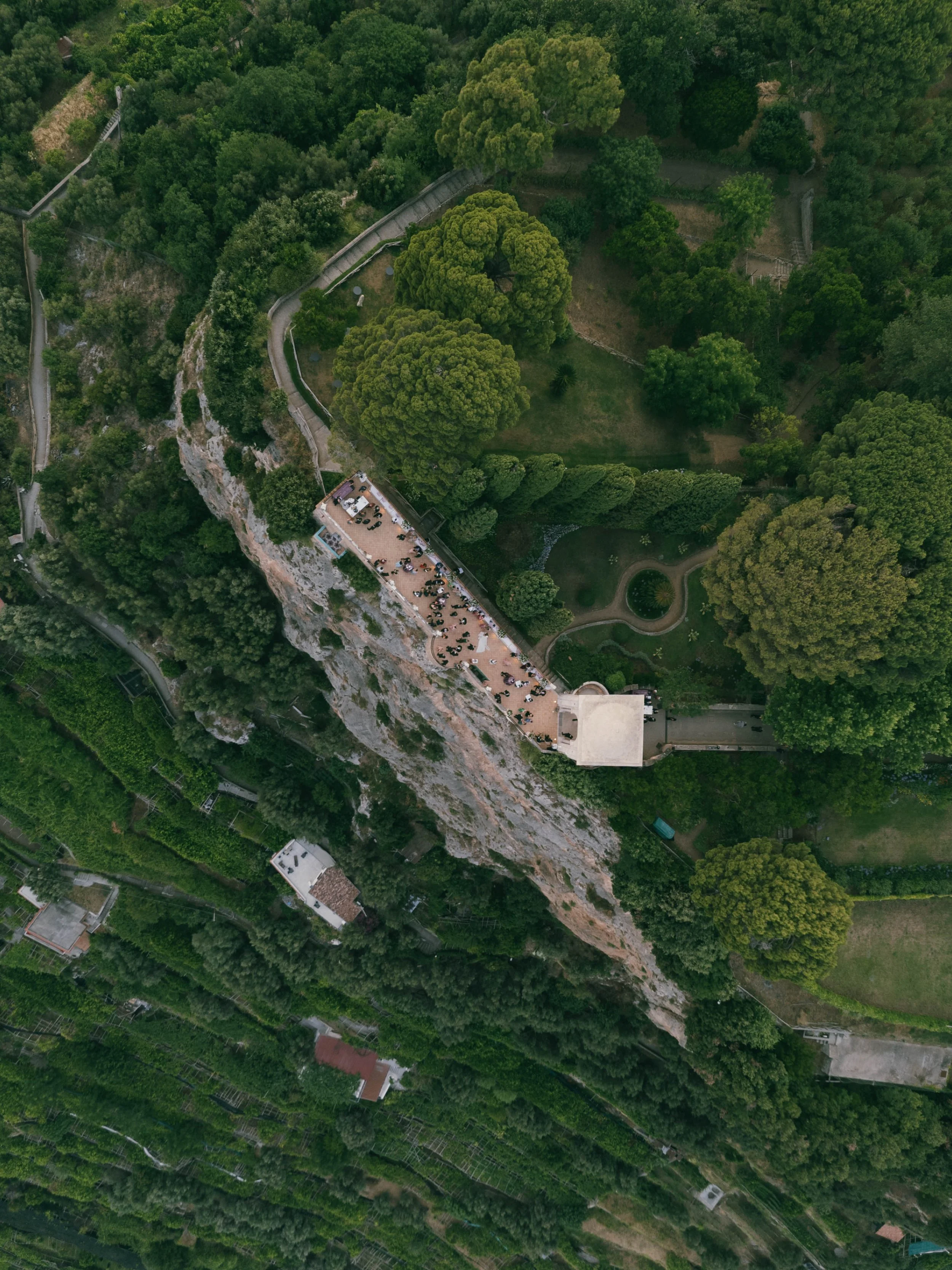 Aerial view of a green landscape with trees, a winding pathway, a small pond, and a building with a rooftop terrace. Villa Cimbrone View, Amalfi Coast Ravello